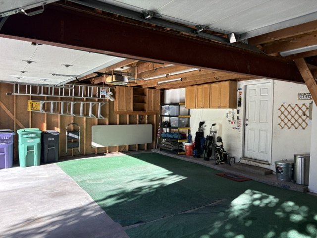 Organized residential garage interior with storage cabinets, bicycles, recycling bins, workbench, and green floor mats