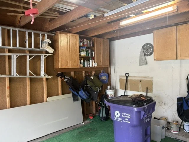 Organized garage interior with wooden cabinets, golf bags, storage shelves, recycling bin, tools, and exposed ceiling beams