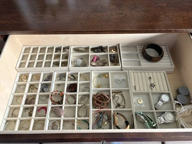 Open wooden jewelry drawer with compartment organizers holding necklaces, bracelets, rings, earrings, watches, and other accessories.