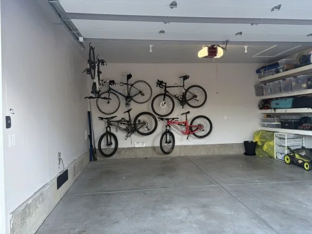 Organized garage with four bicycles mounted on the back wall, storage shelves, and lawn equipment.