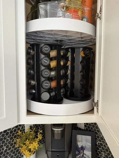 Rotating spice rack filled with labeled spice jars inside a white kitchen cabinet