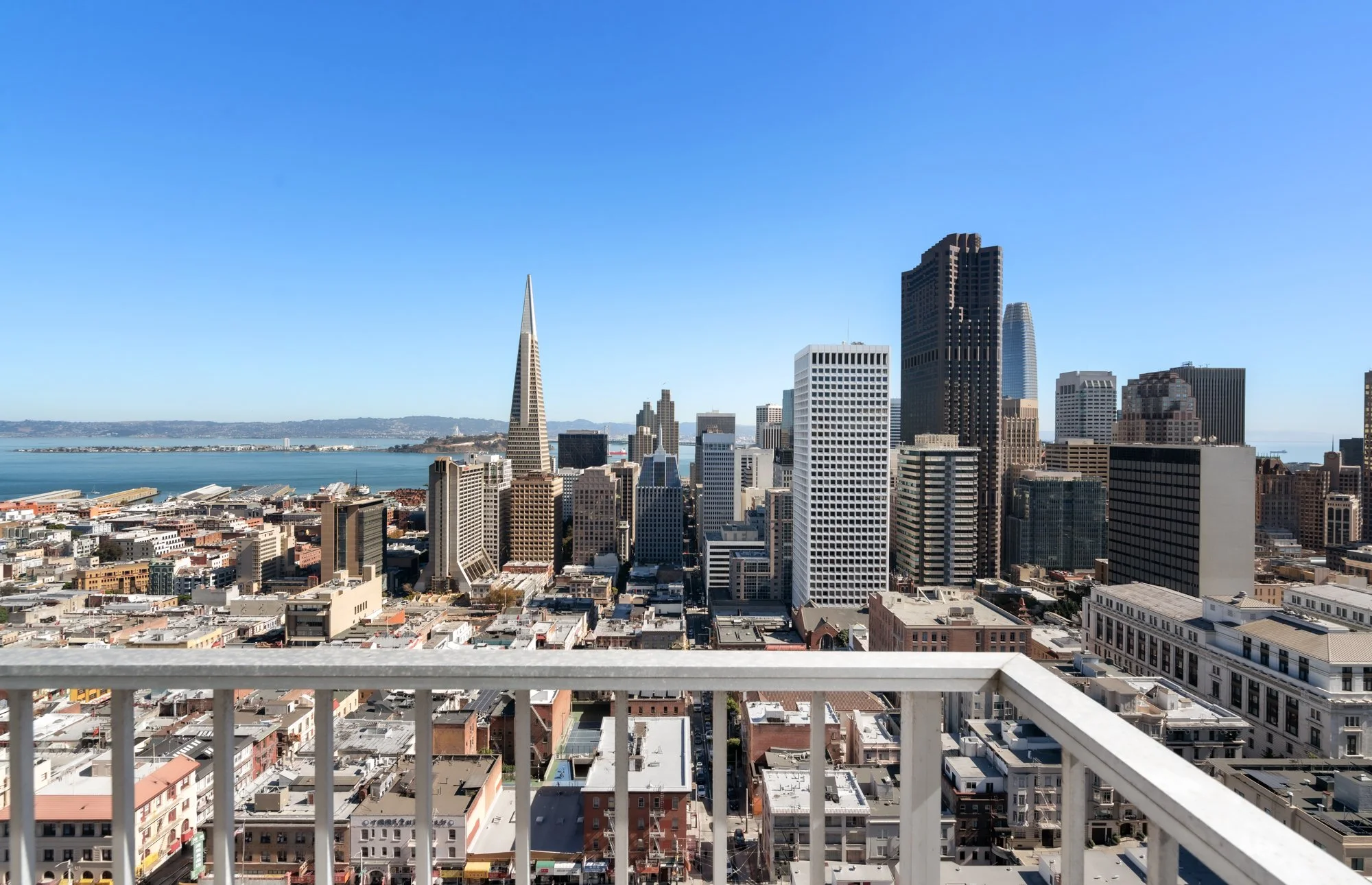 View of San Francisco skyline with iconic Transamerica Pyramid and surrounding tall buildings, overlooking the bay, seen from a balcony with a railing.