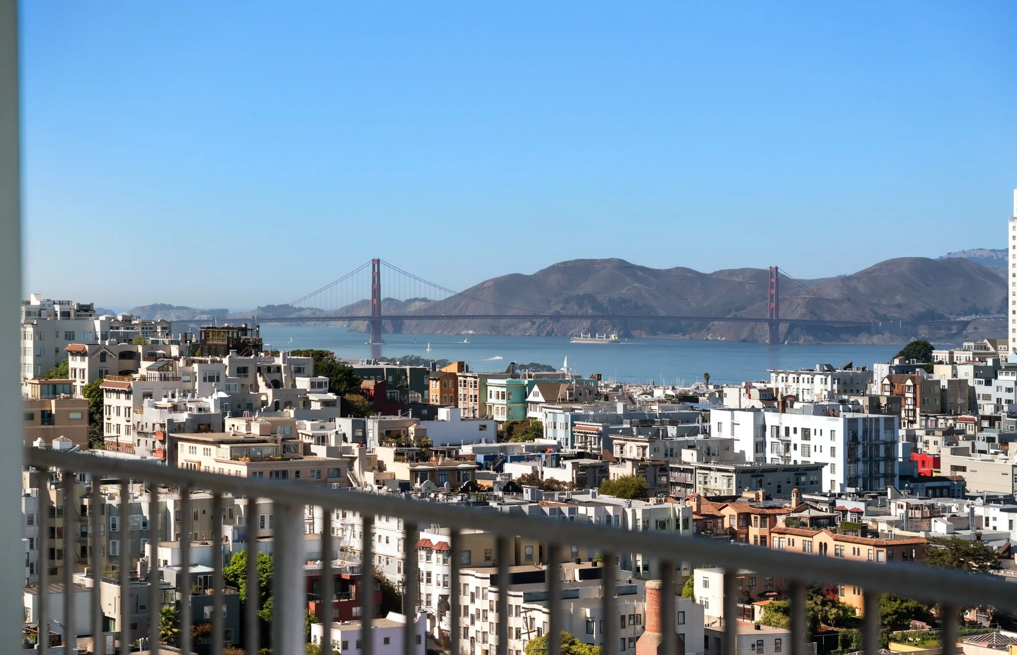 Cityscape view of San Francisco with colorful buildings in the foreground and the Golden Gate Bridge in the background under a clear blue sky.