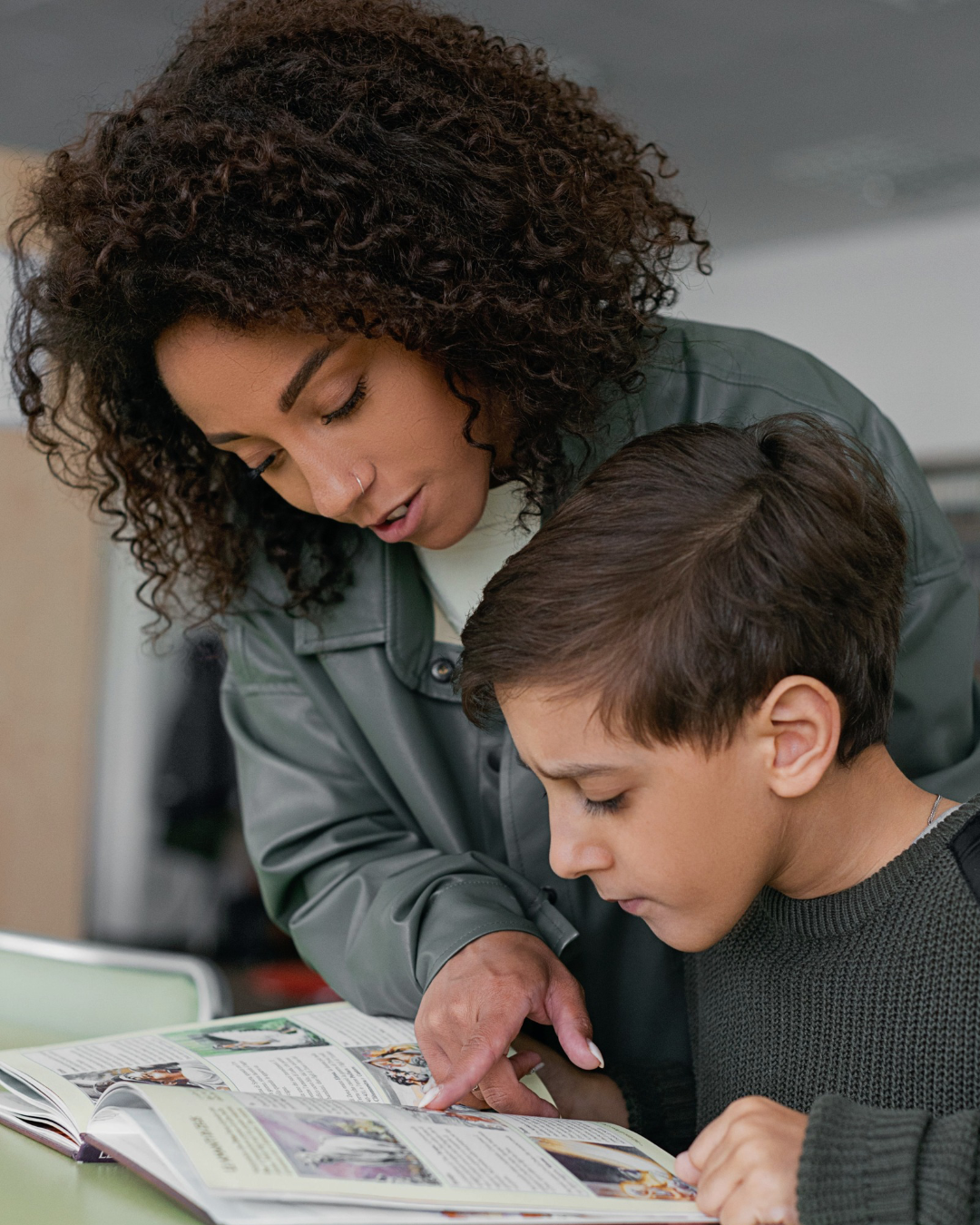 A woman and a young boy looking at a magazine or book together, with the woman pointing at something on the page.