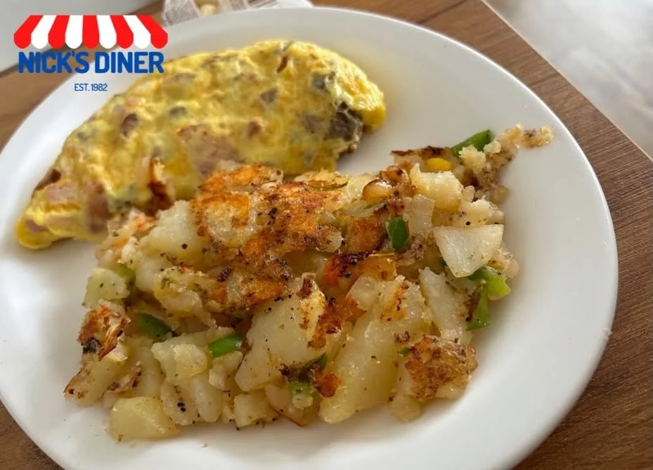 A plate with an omelette and home fries. The omelette contains ham and cheese, and the home fries are topped with onions and green peppers.