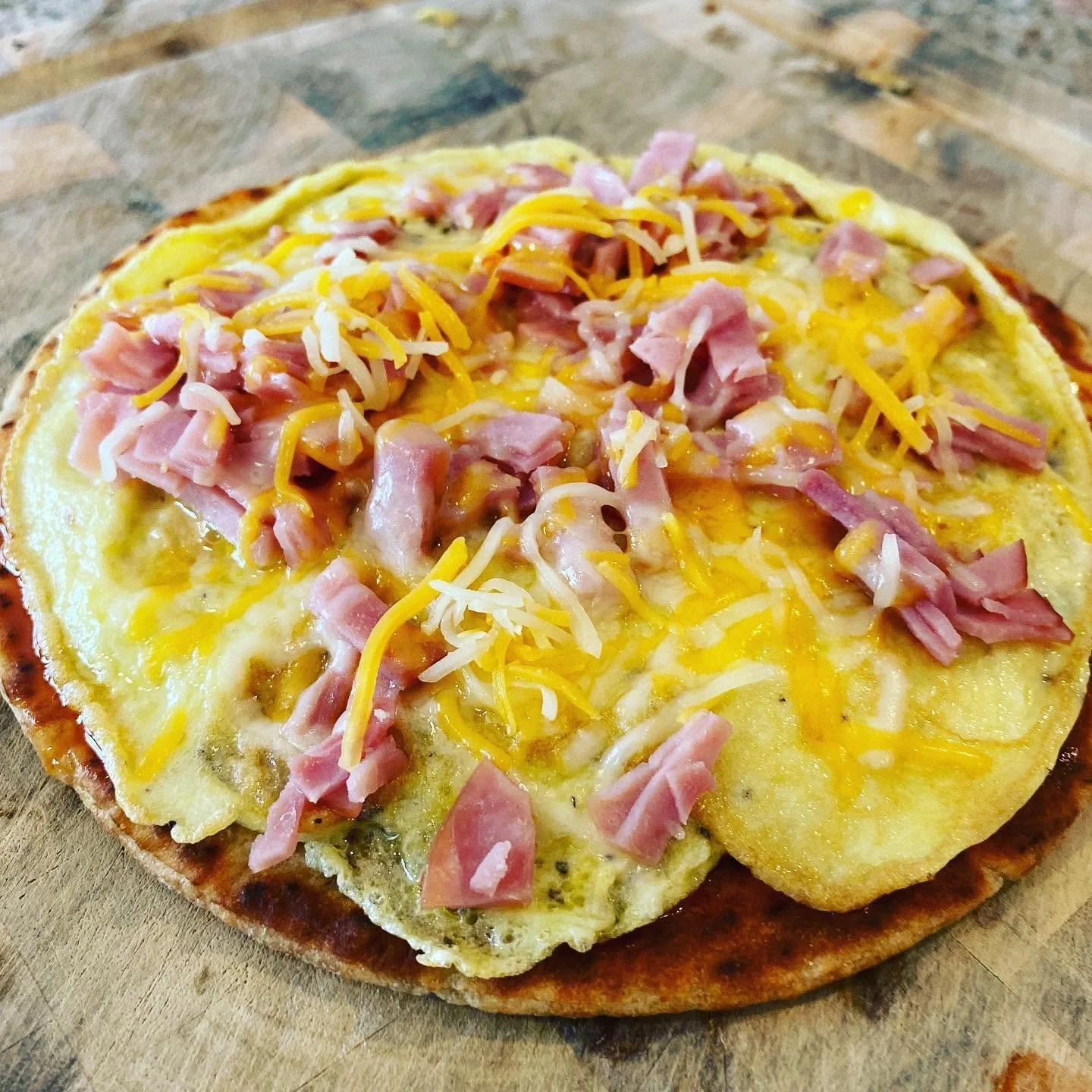 Close-up of a homemade pizza with cheese, ham, and potato slices on a wooden surface.