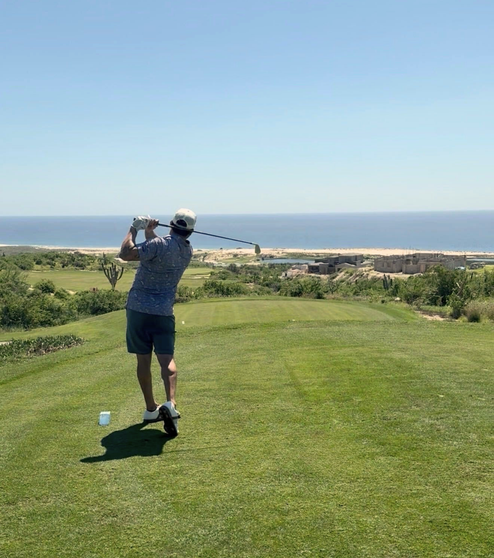 Golfer swinging a club on a coastal golf course overlooking the ocean