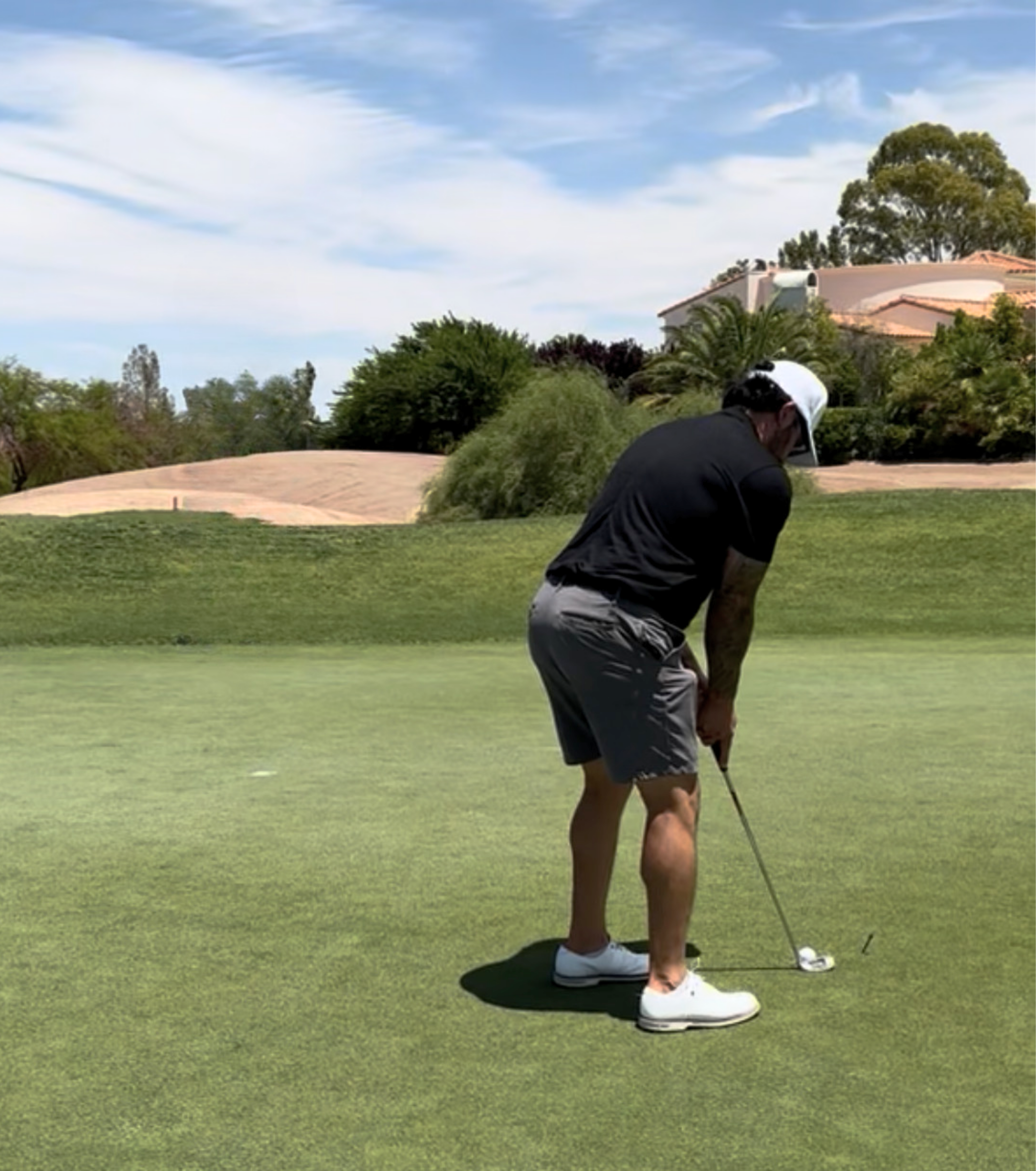 Golfer preparing to putt on a sunny golf course near a Mediterranean-style home