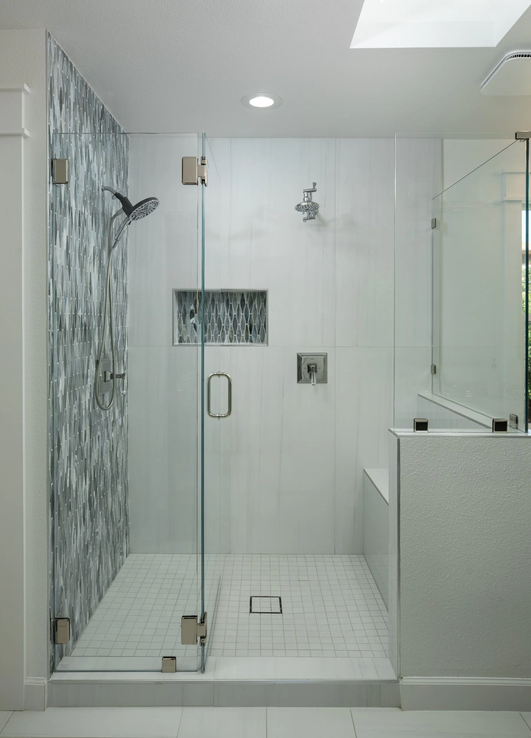 A modern walk-in shower with glass doors, a rain shower head, a handheld shower, and a built-in niche with decorative tiles.