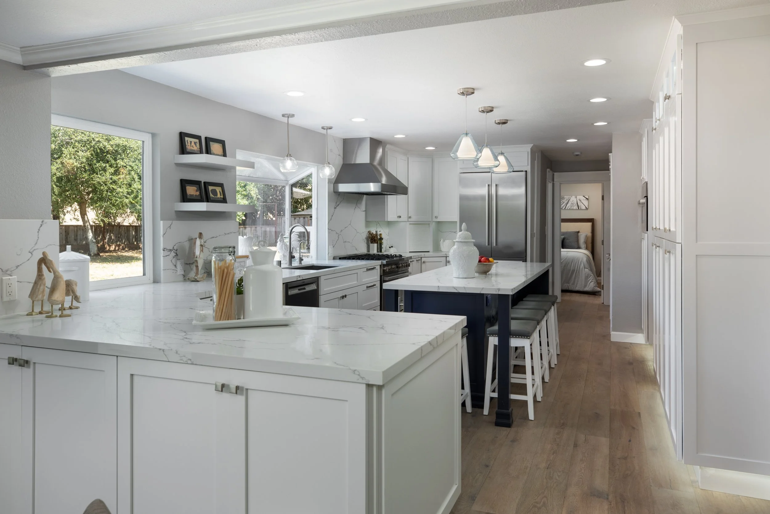 Modern white kitchen with stainless steel appliances, and a breakfast bar with stools.
