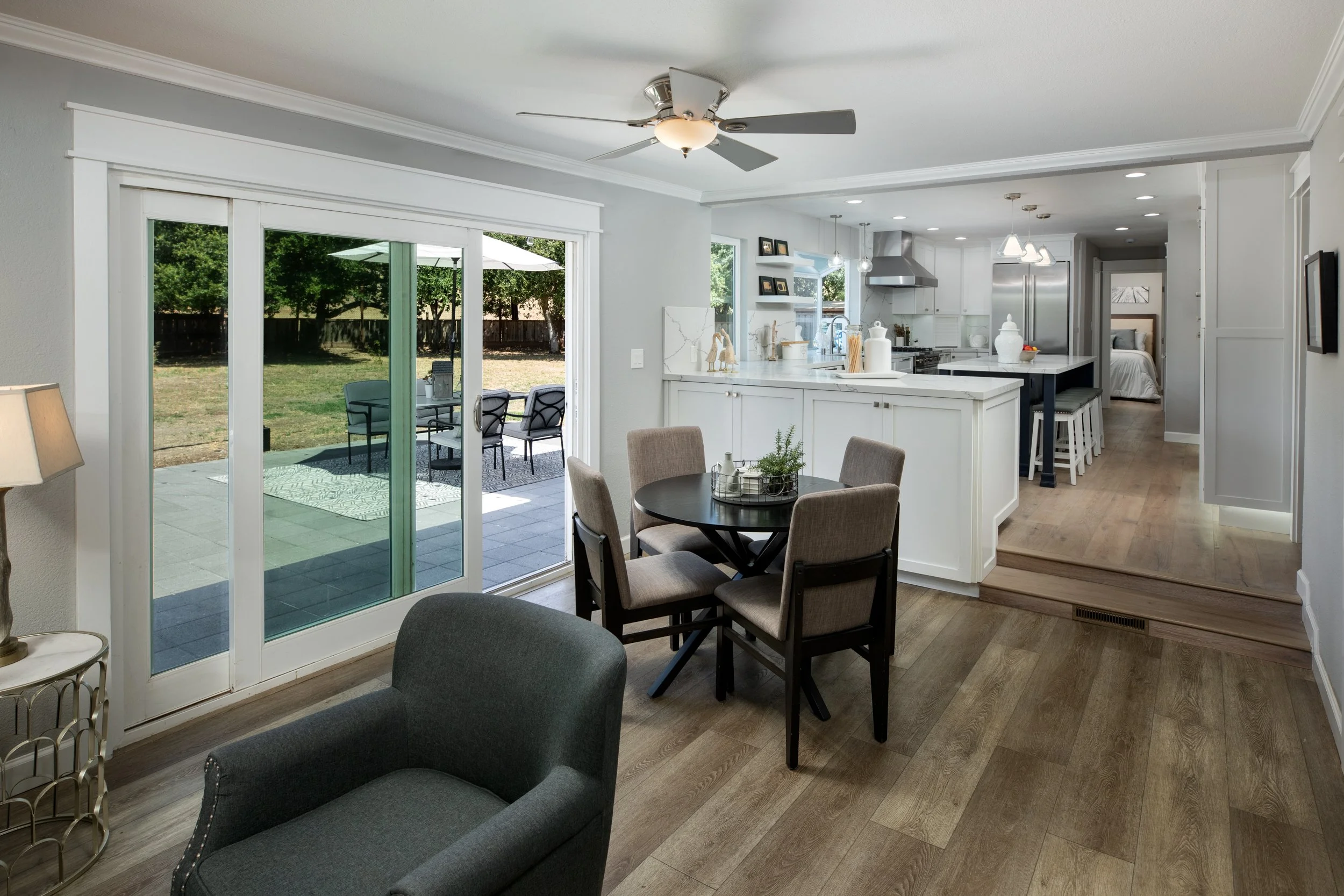 Open-concept living and kitchen area with sliding glass door leading to a backyard with patio furniture and trees.