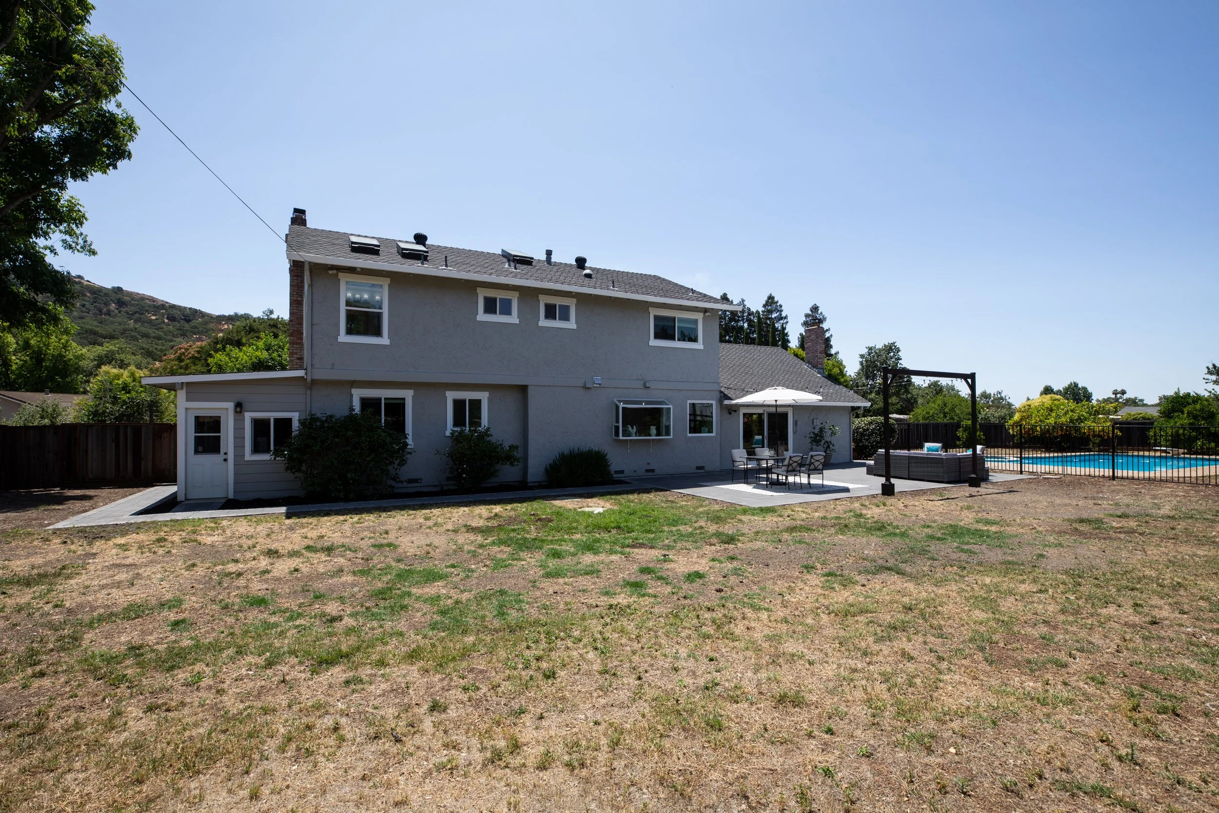 Backyard with two-story house, patio furniture, and a swimming pool enclosed by a black fence.