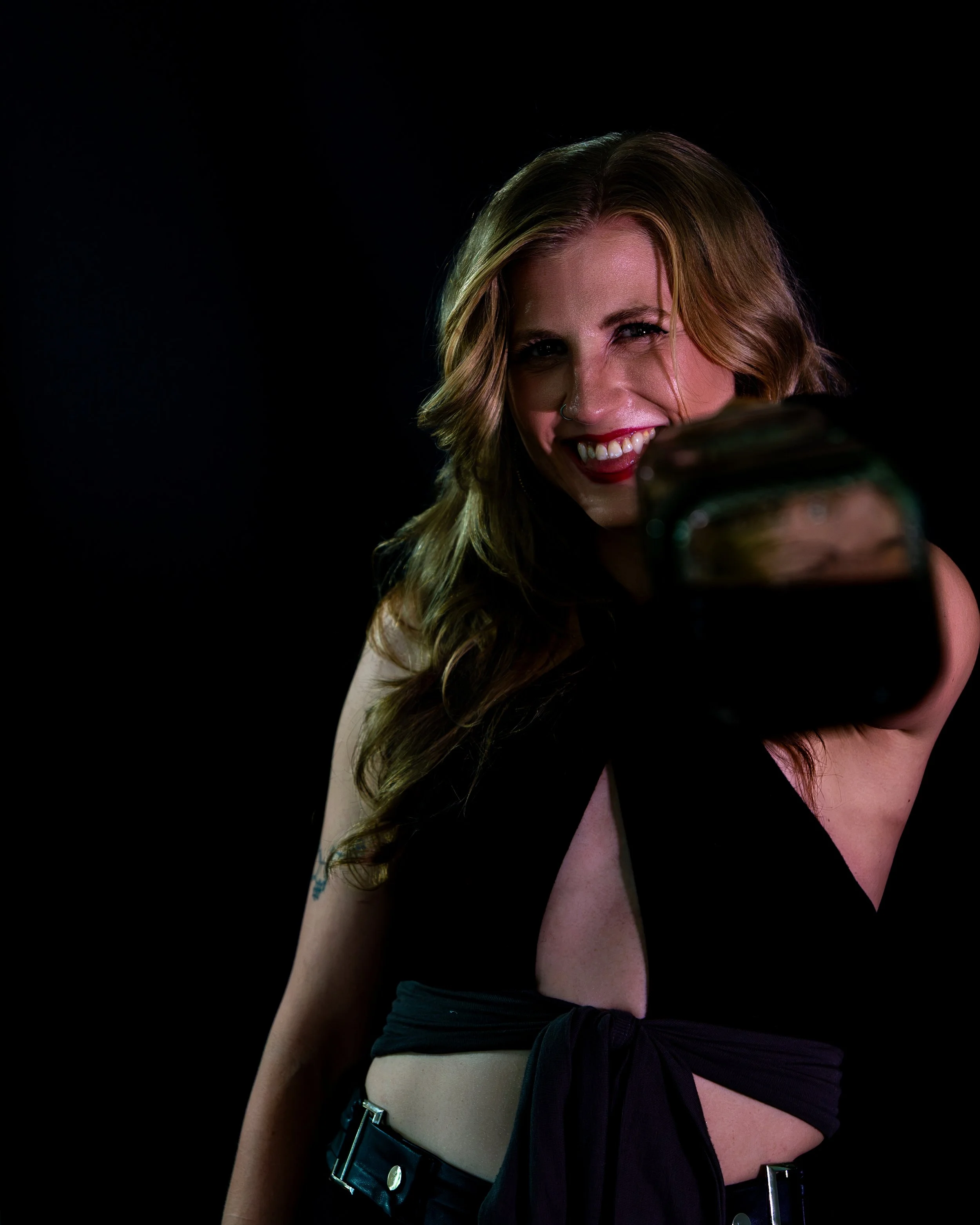 Smiling woman with long hair and a nose ring posing against a black background