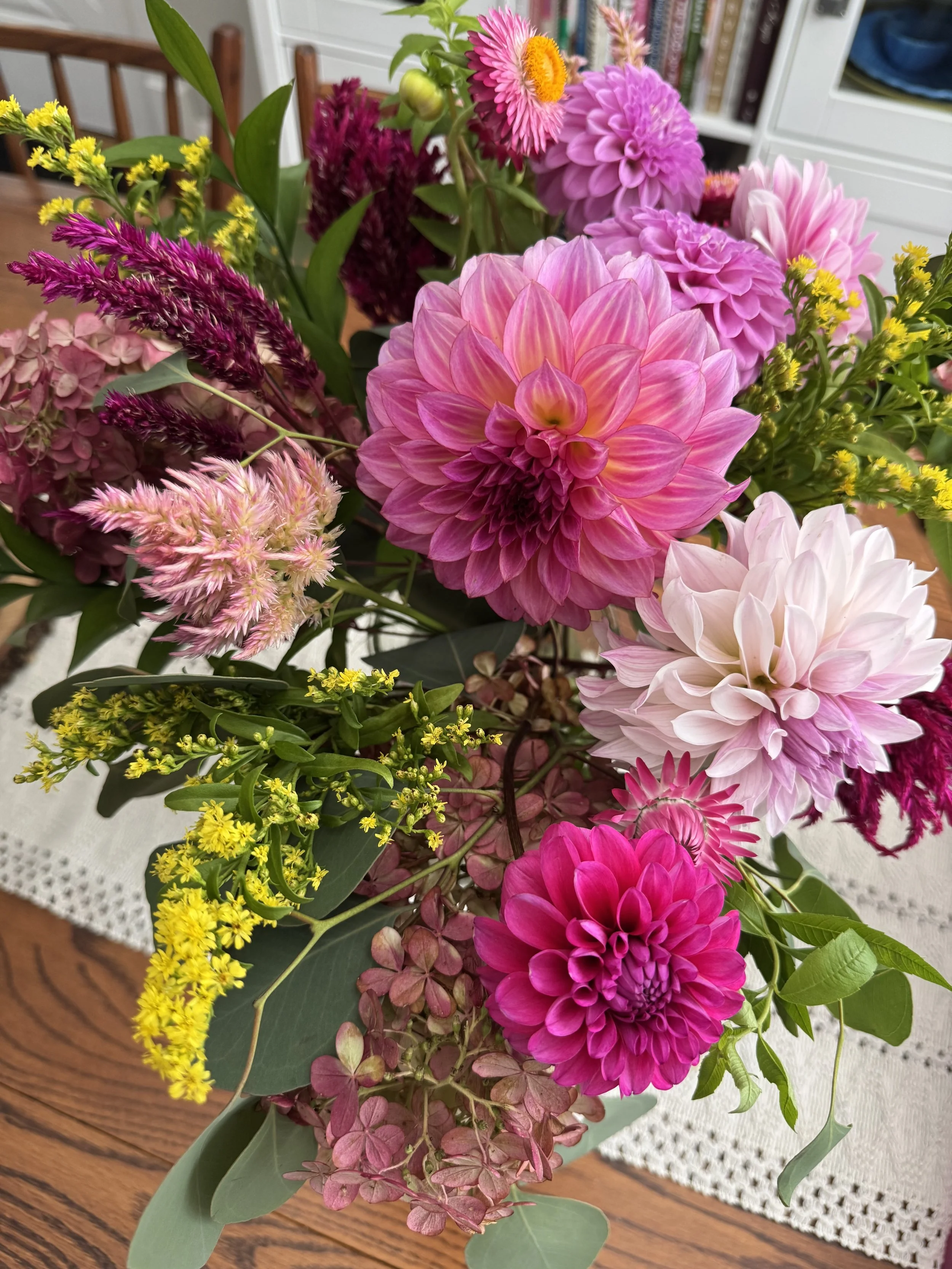 A vibrant bouquet of pink, purple, yellow, and white flowers with green leaves on a wooden table.