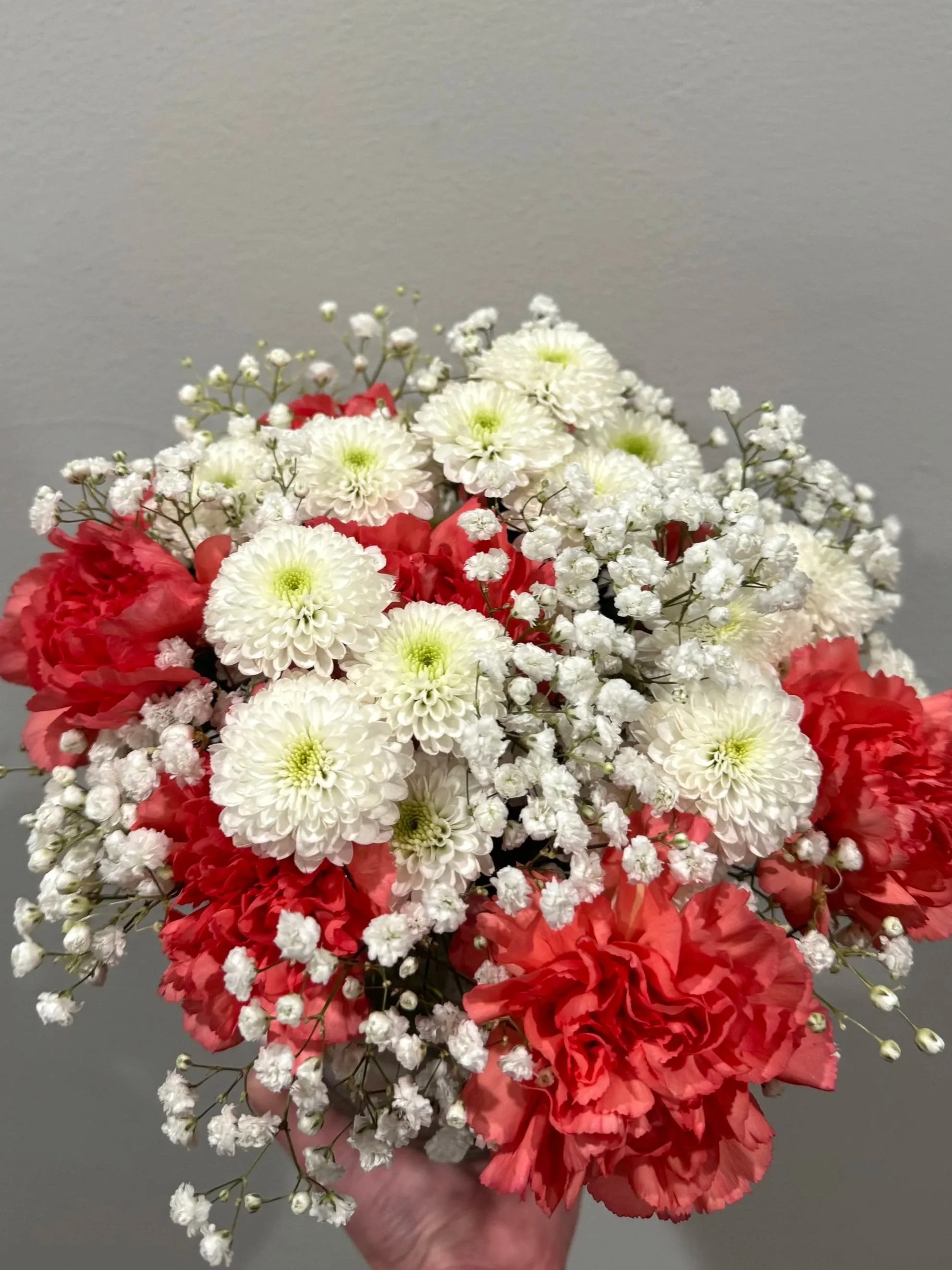 Bouquet of white, red, and pink flowers held in a person's hand against a plain background.