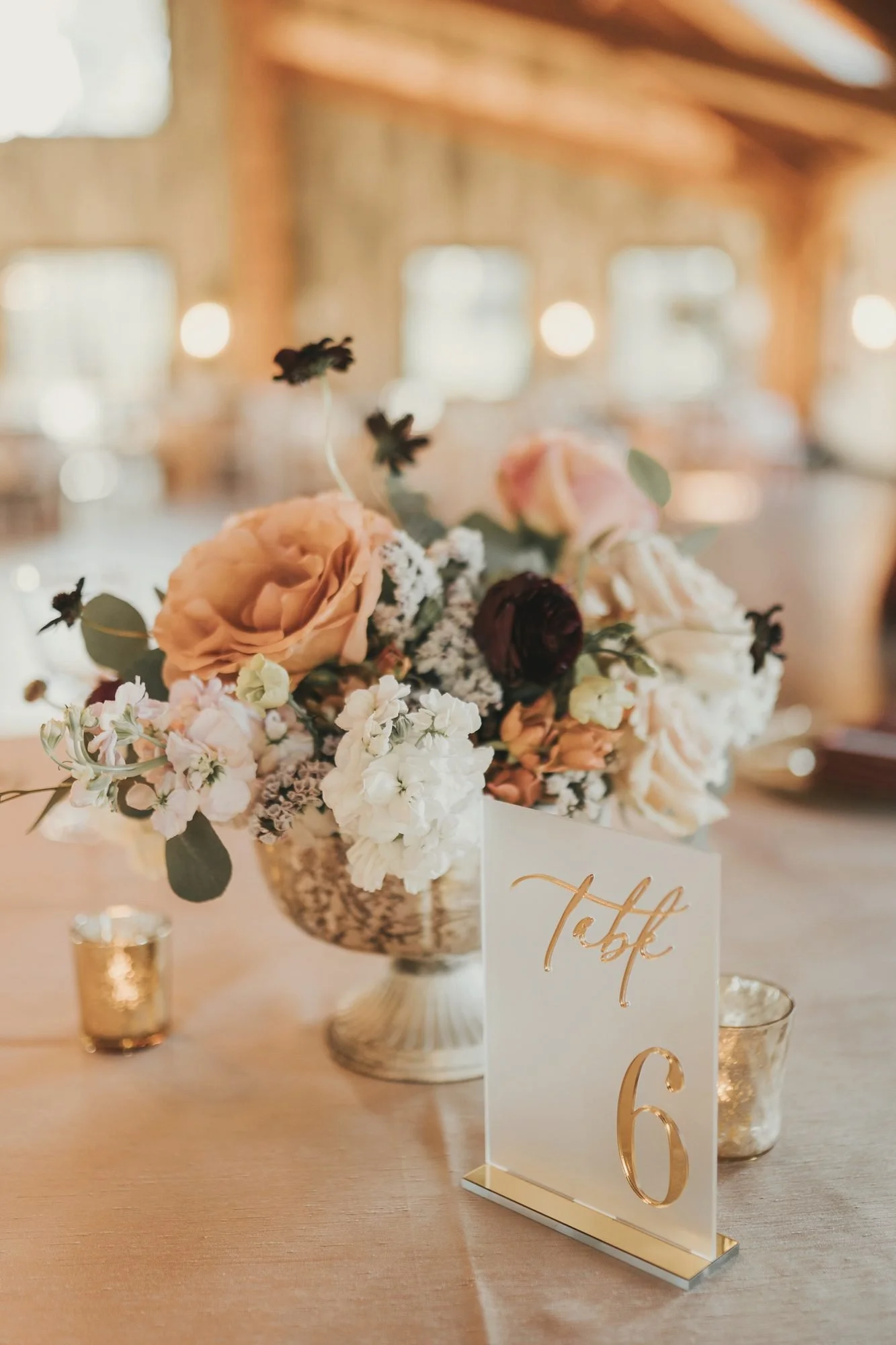 Peach rose and ivory centerpiece beside a frosted acrylic table number with gold script