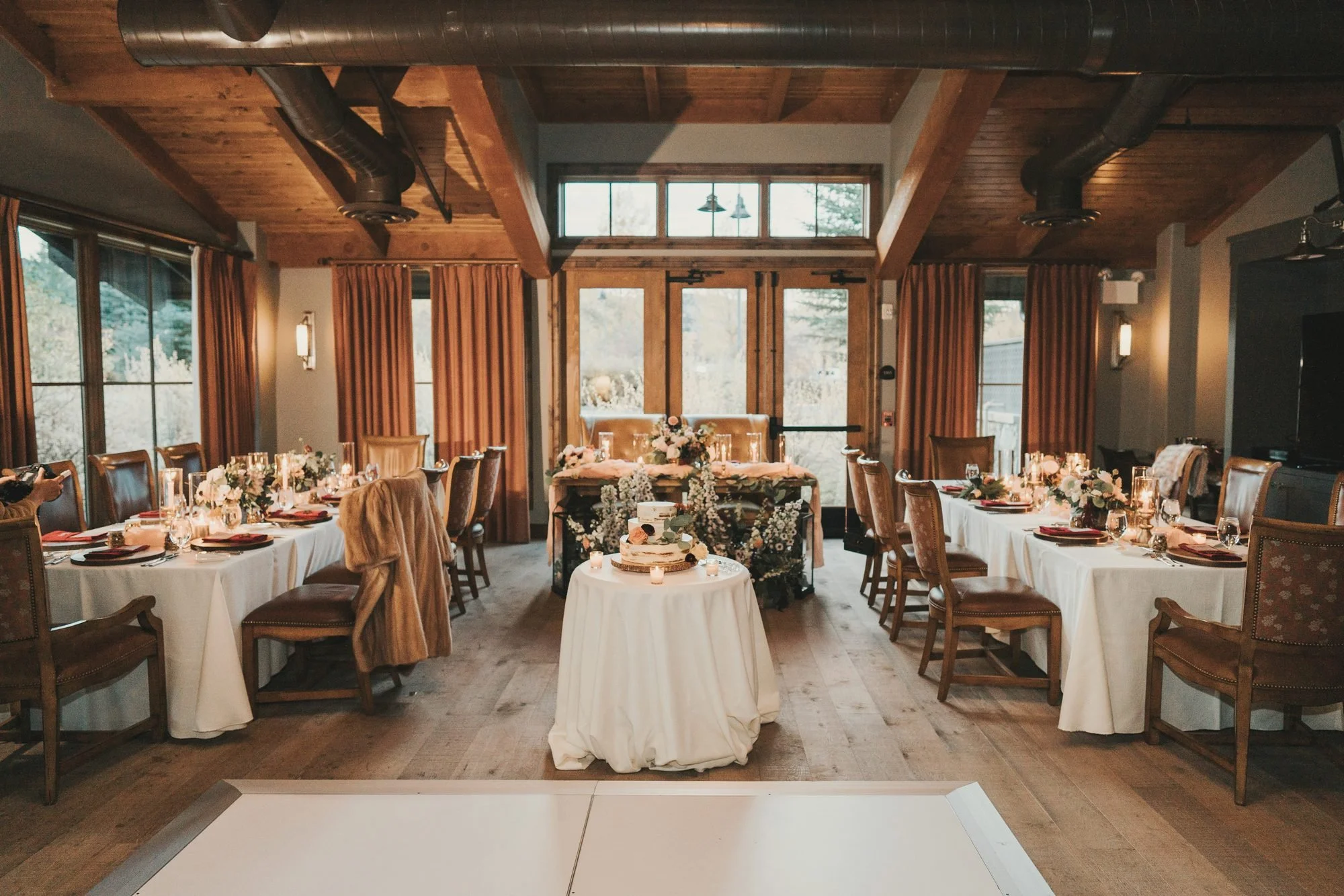Warm mountain lodge reception room with long candlelit tables and a centered wedding cake