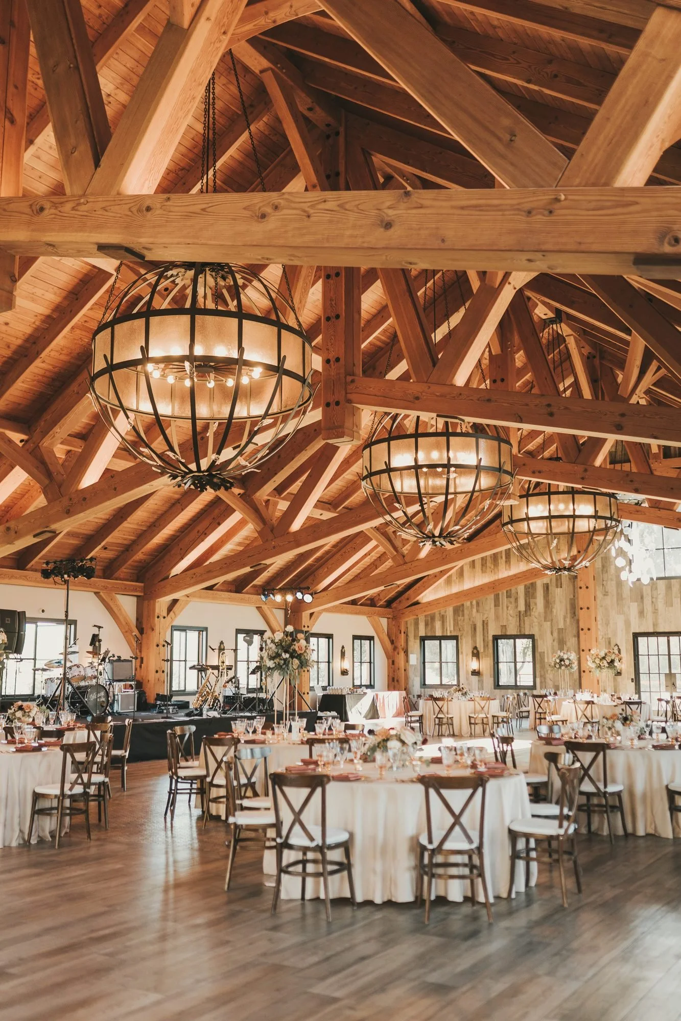 Grand barn reception hall with iron globe chandeliers, ivory linens and crossback chairs