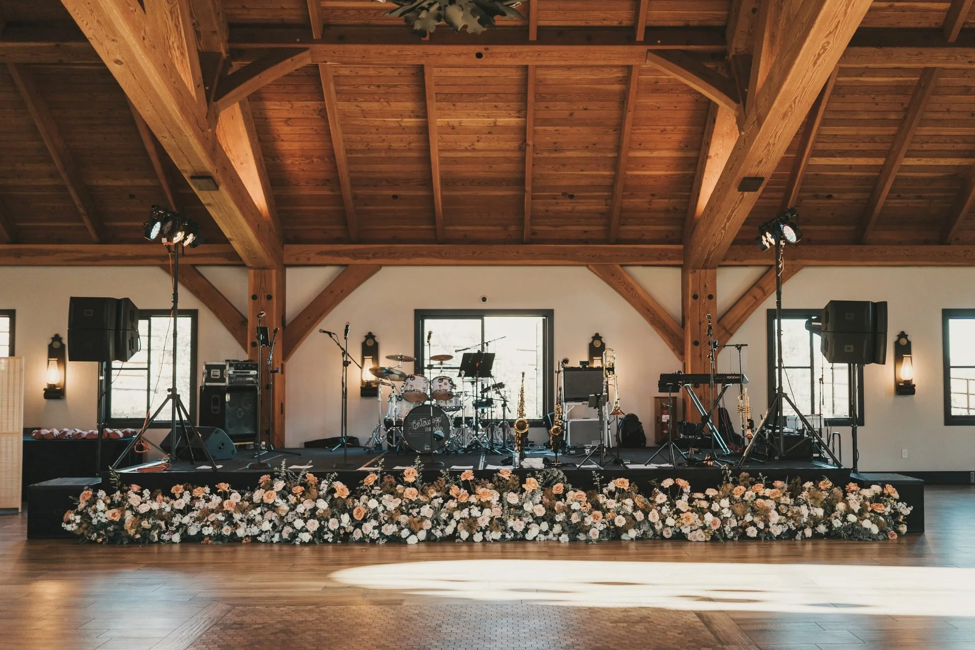 Barn reception stage with a lush peach and white floral riser beneath warm timber beams