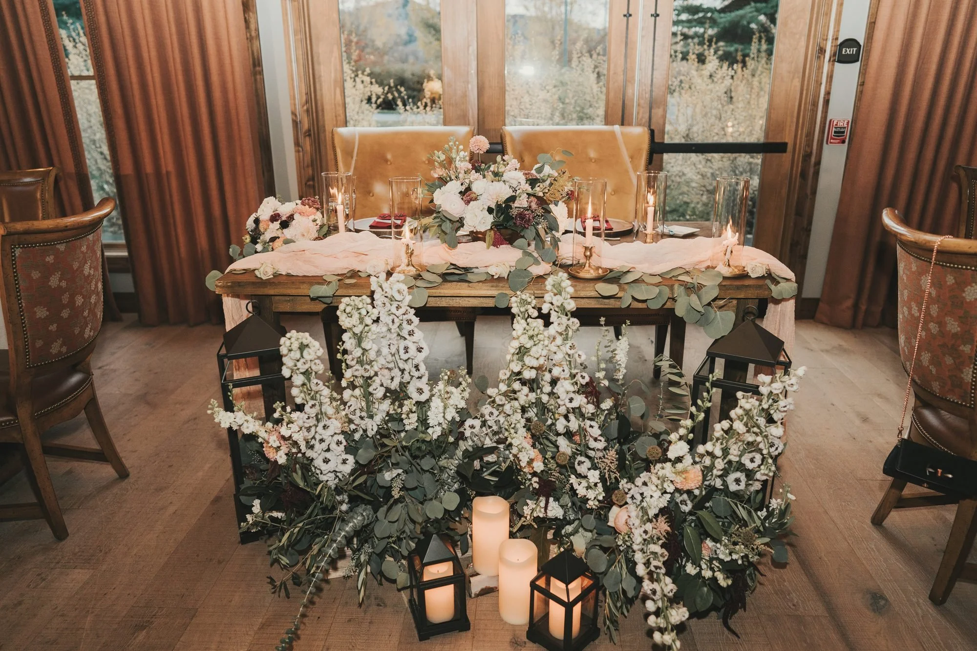 Mountain lodge sweetheart table with cascading white delphinium, eucalyptus, lanterns and candlelight