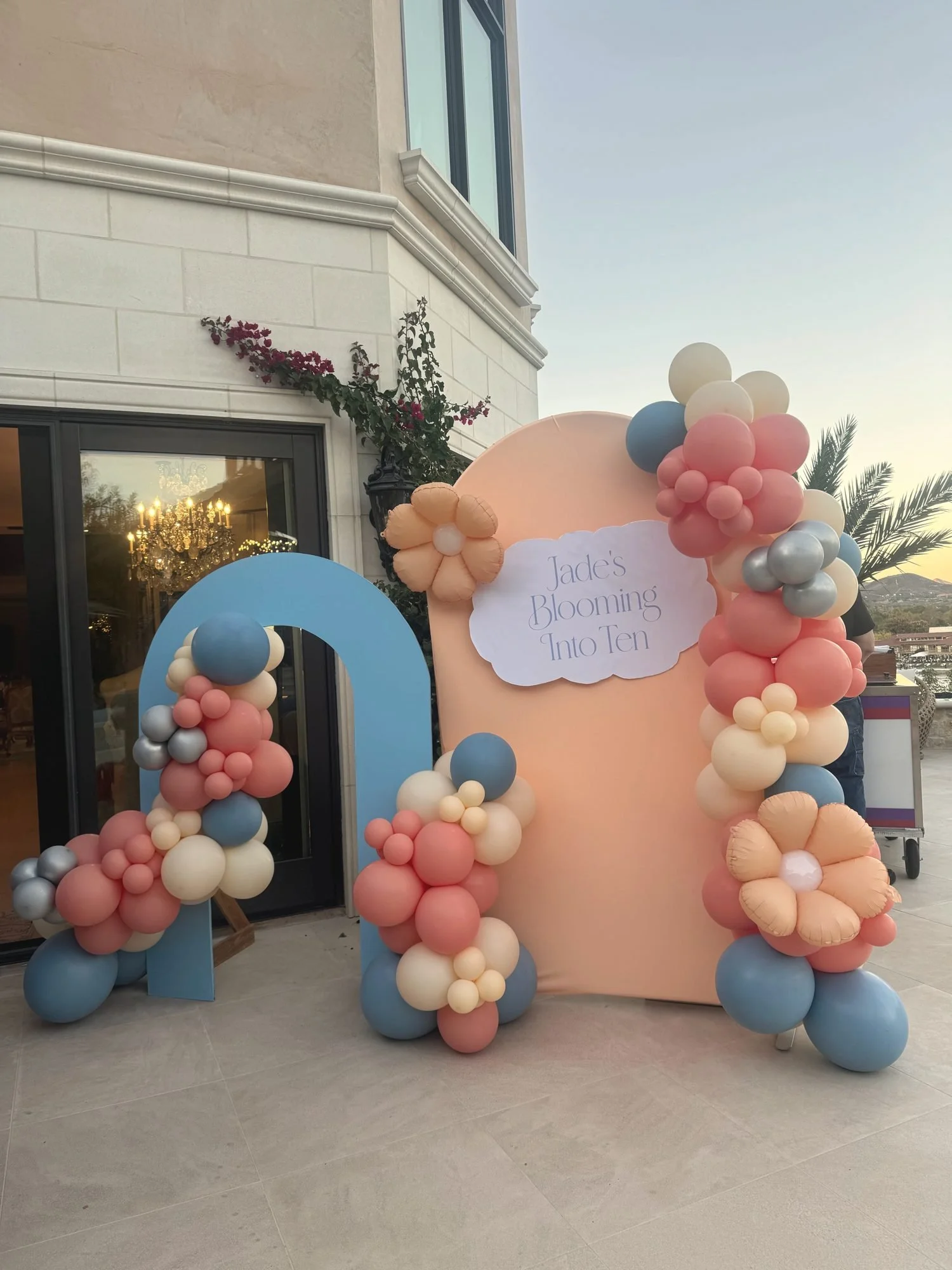 Peach and blue balloon garland with daisy balloons framing a Blooming Into Ten birthday backdrop
