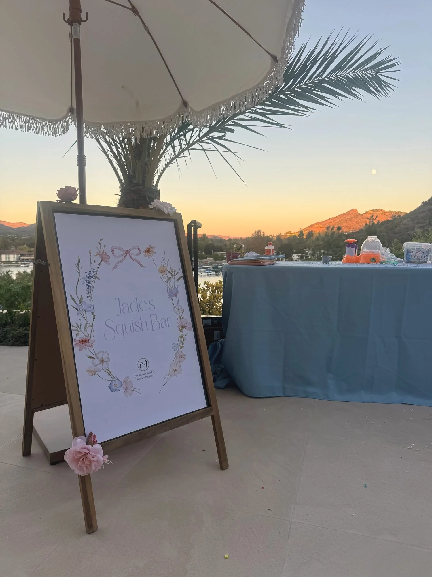 Squish Bar sign with watercolor florals beside a blue-draped table at sunset