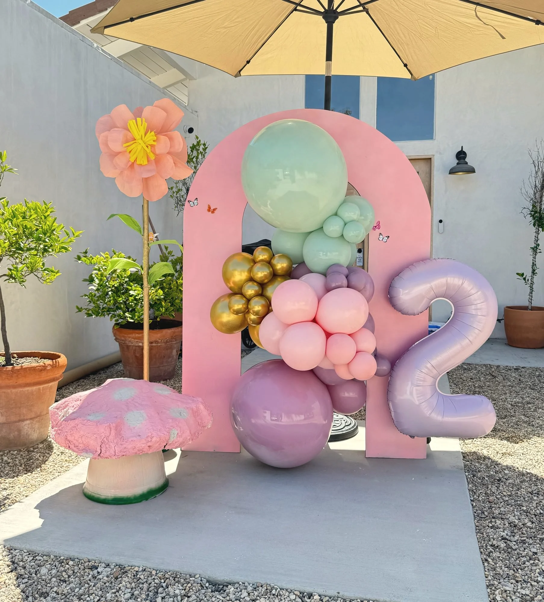 Pink arch with sage, pink and gold balloons and a mushroom prop