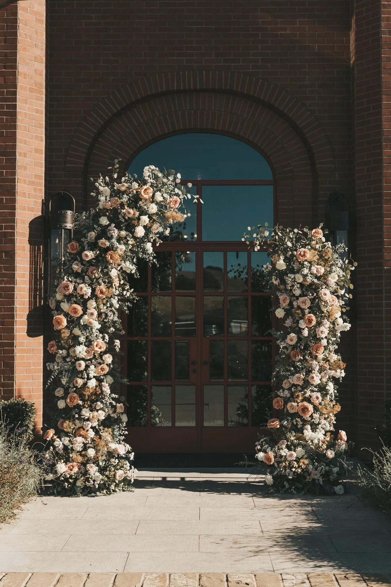 Peach and ivory floral columns framing an arched brick doorway in afternoon sun