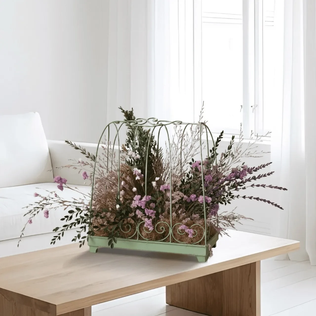 Green vintage metal planter filled with dried pink and purple flowers on a light wood table in a bright white room