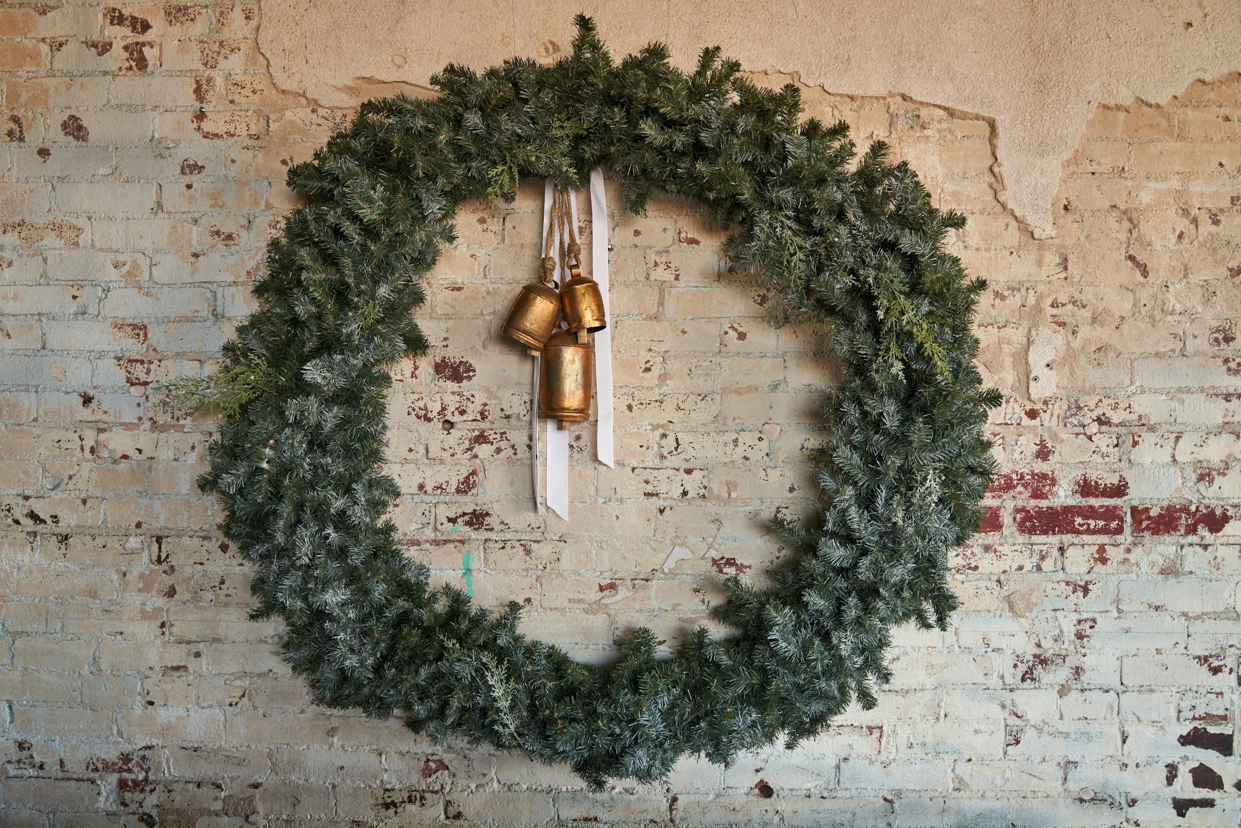 Christmas wreath with bronze bells and white ribbons on a rustic exposed brick wall