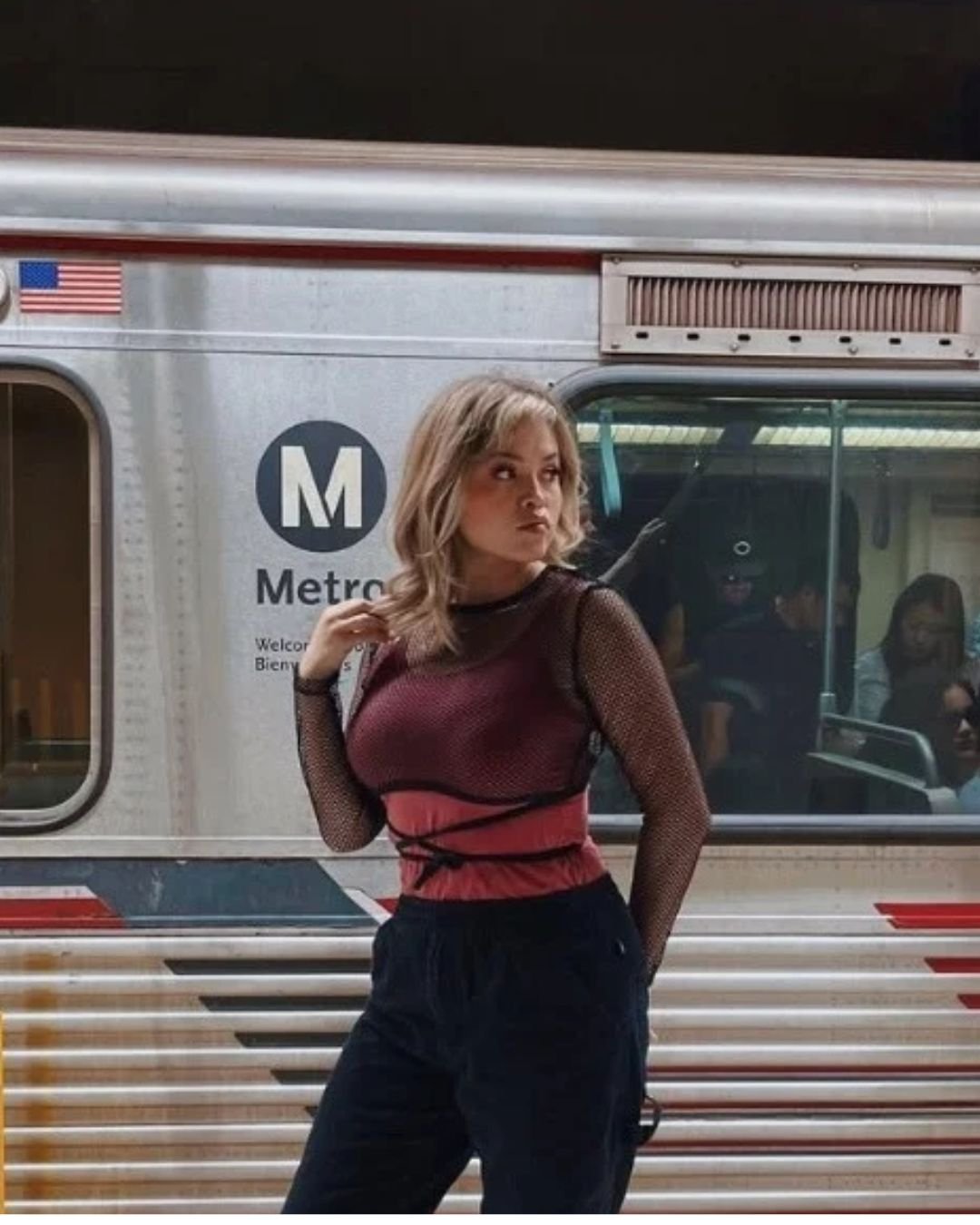 Woman posing in front of a silver Metro subway train with an American flag and Metro logo