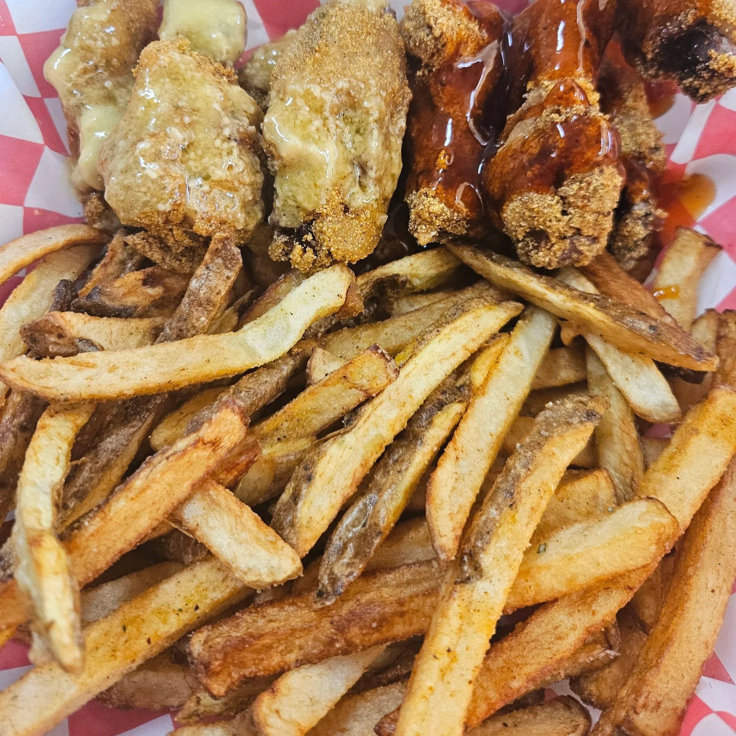 Close-up of seasoned roasted chicken wings served with French fries, drizzled with gravy and sauce.