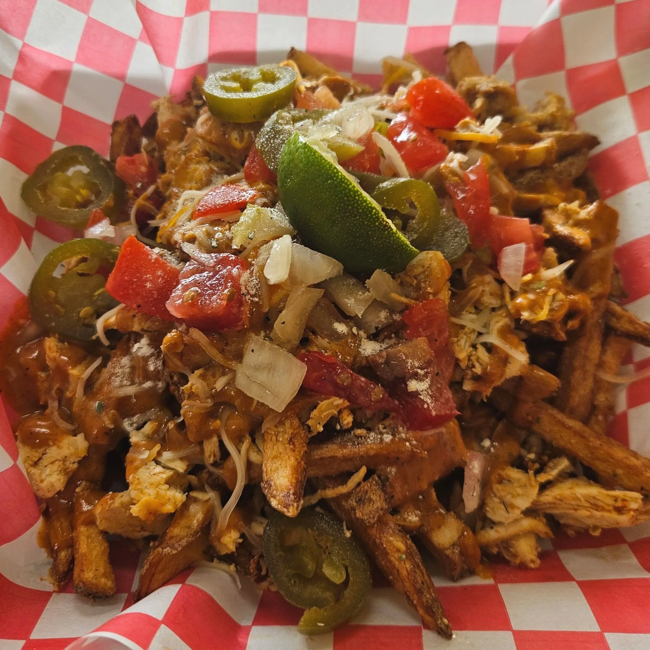 Close-up of a basket filled with cooked and seasoned chicken strips, green jalapeño slices, and shredded cheese on a red and white checkered paper lining.