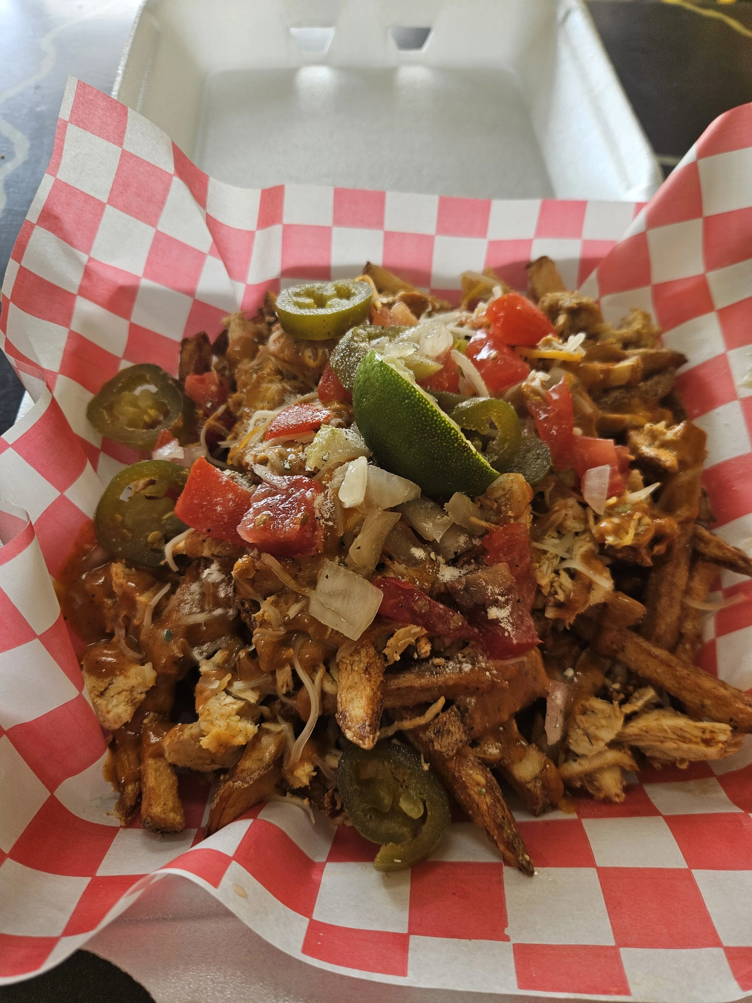 Close-up of a loaded plate of Mexican food including jalapeños, shredded cheese, diced tomatoes, onion, and seasoned meat, served in a red and white checkered paper-lined basket.