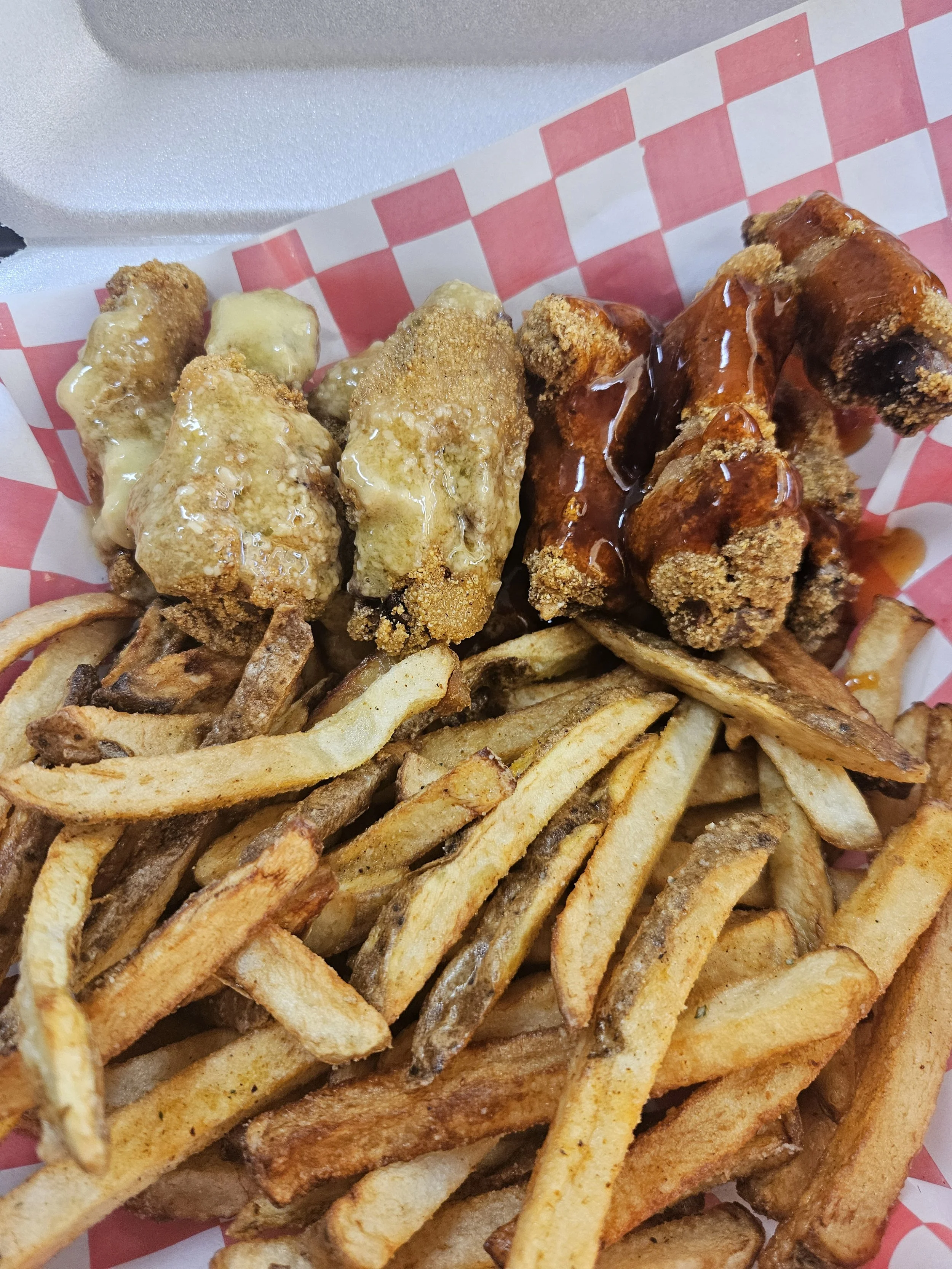 Fried chicken tenders with honey mustard sauce and barbecue sauce, served with French fries on a red and white checkered paper-lined basket.