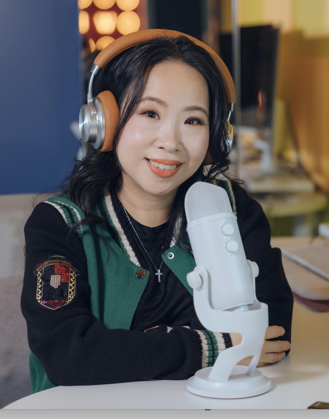Smiling woman wearing orange headphones and speaking into a white desktop microphone