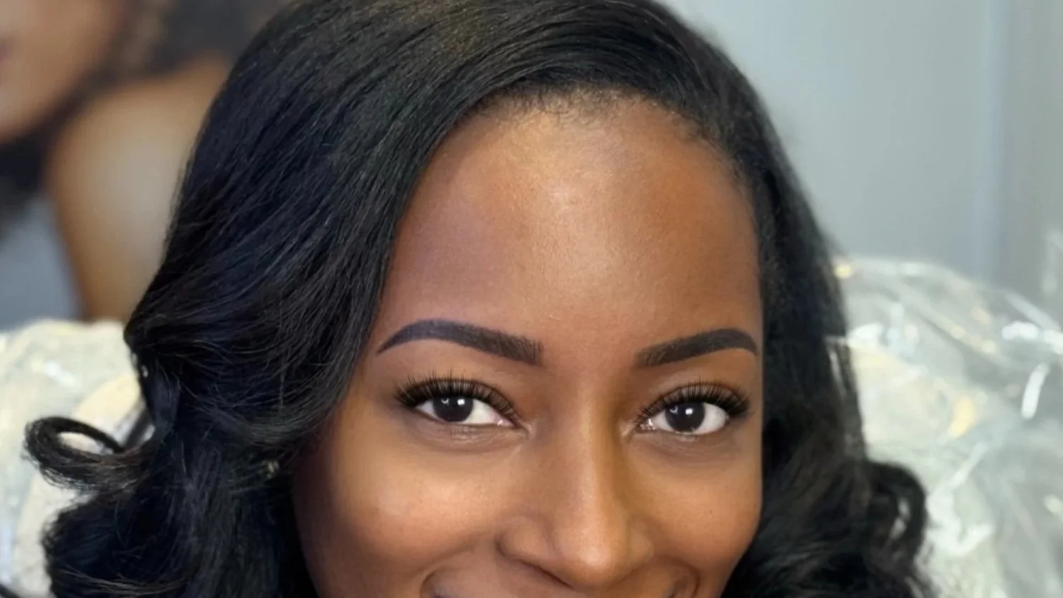 Close-up of a smiling African American woman with styled black wavy hair and makeup, looking at the camera.