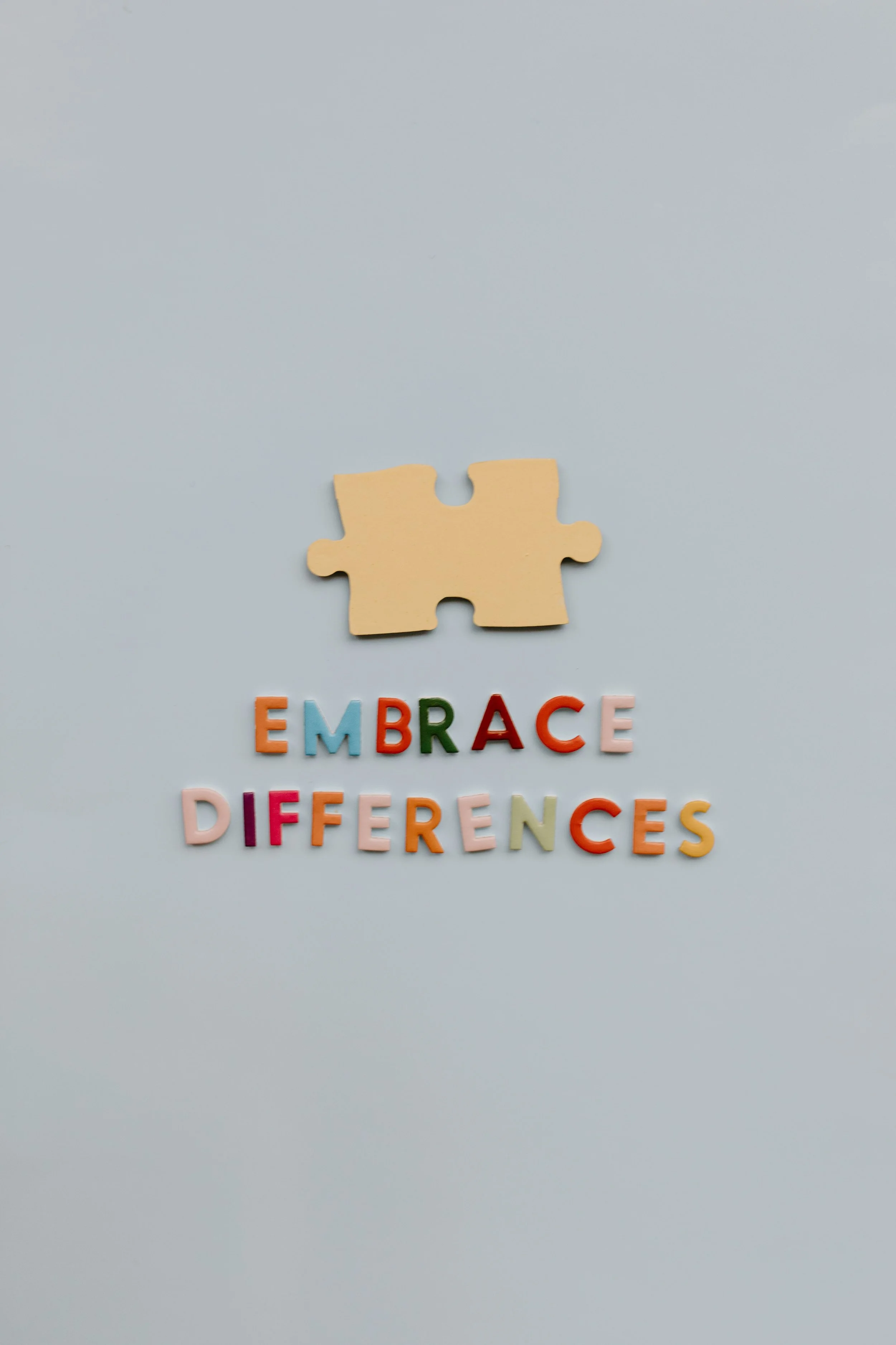 A yellow puzzle piece situated above colorful letters spelling out the words 'EMBRACE DIVERSENCES' referring to ADHD and autism on a light background.