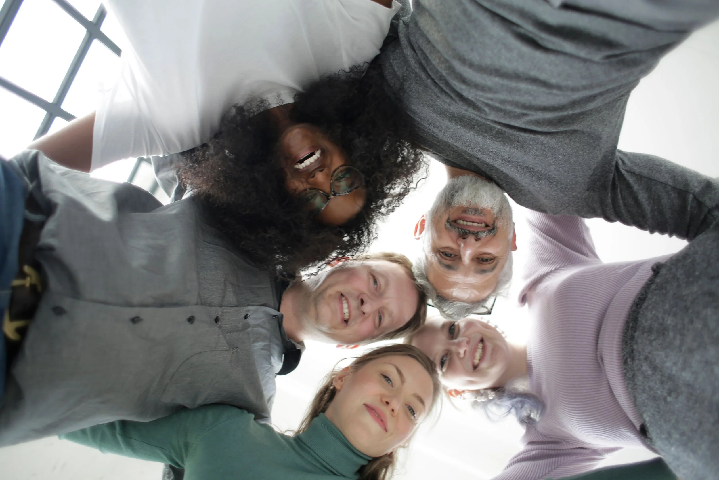 Group of diverse people smiling and taking a selfie from below, looking down into the camera.