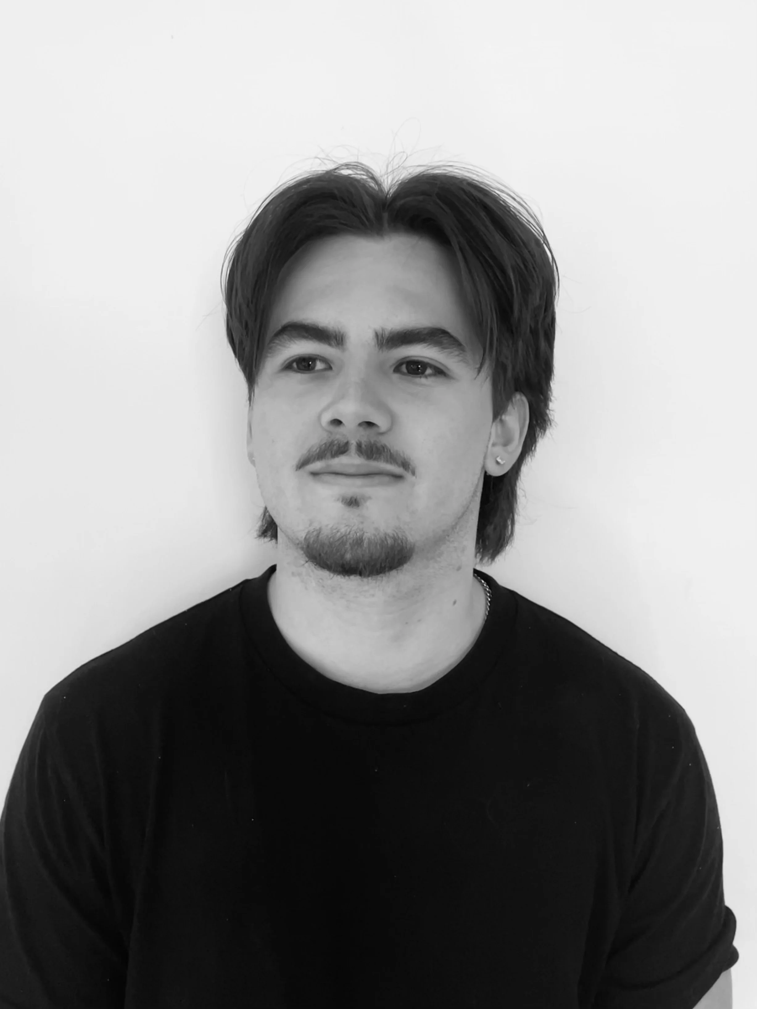 Black-and-white head-and-shoulders portrait of a man with dark hair, mustache, beard, and an earring wearing a black shirt