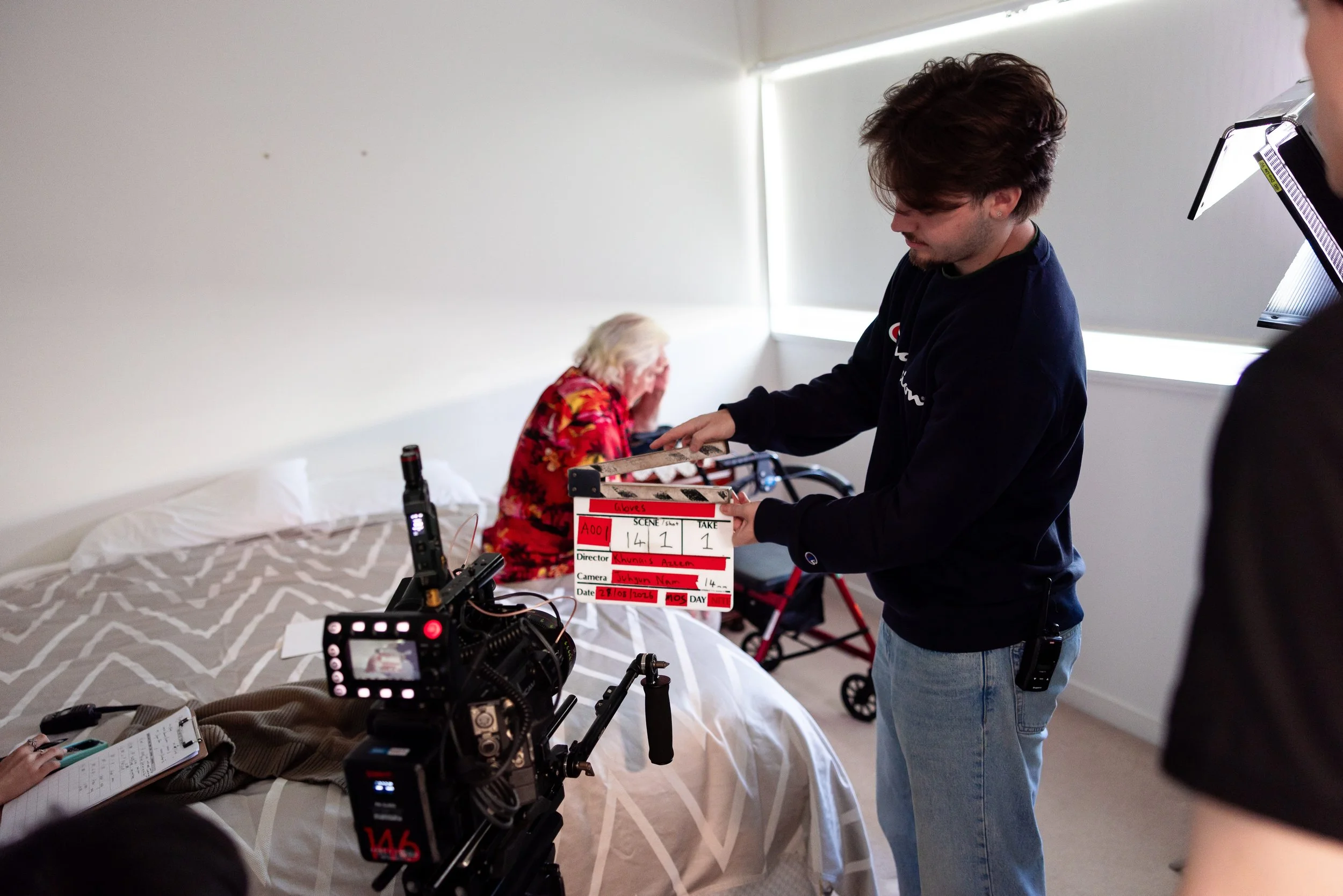Film crew member holding a clapperboard beside a camera filming a child in a bedroom set