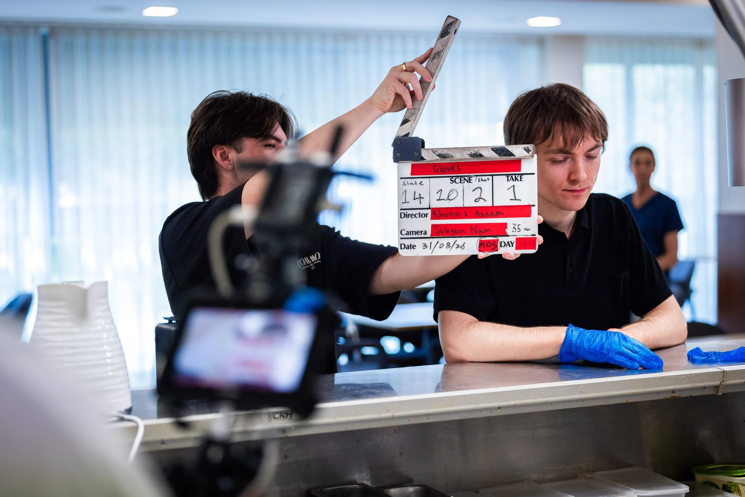 Film crew member holding a clapperboard beside a seated actor wearing a blue glove on set