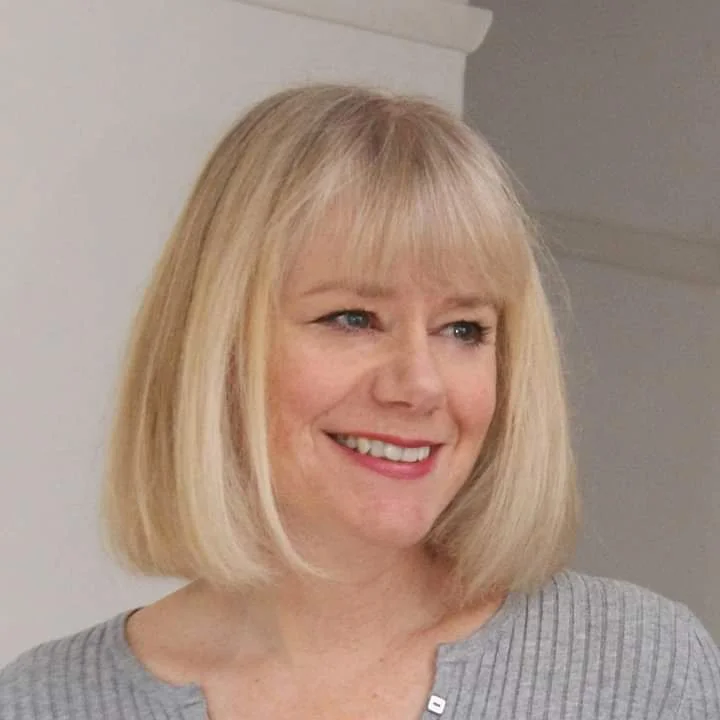 Smiling woman with blonde bob haircut and bangs wearing a gray sweater