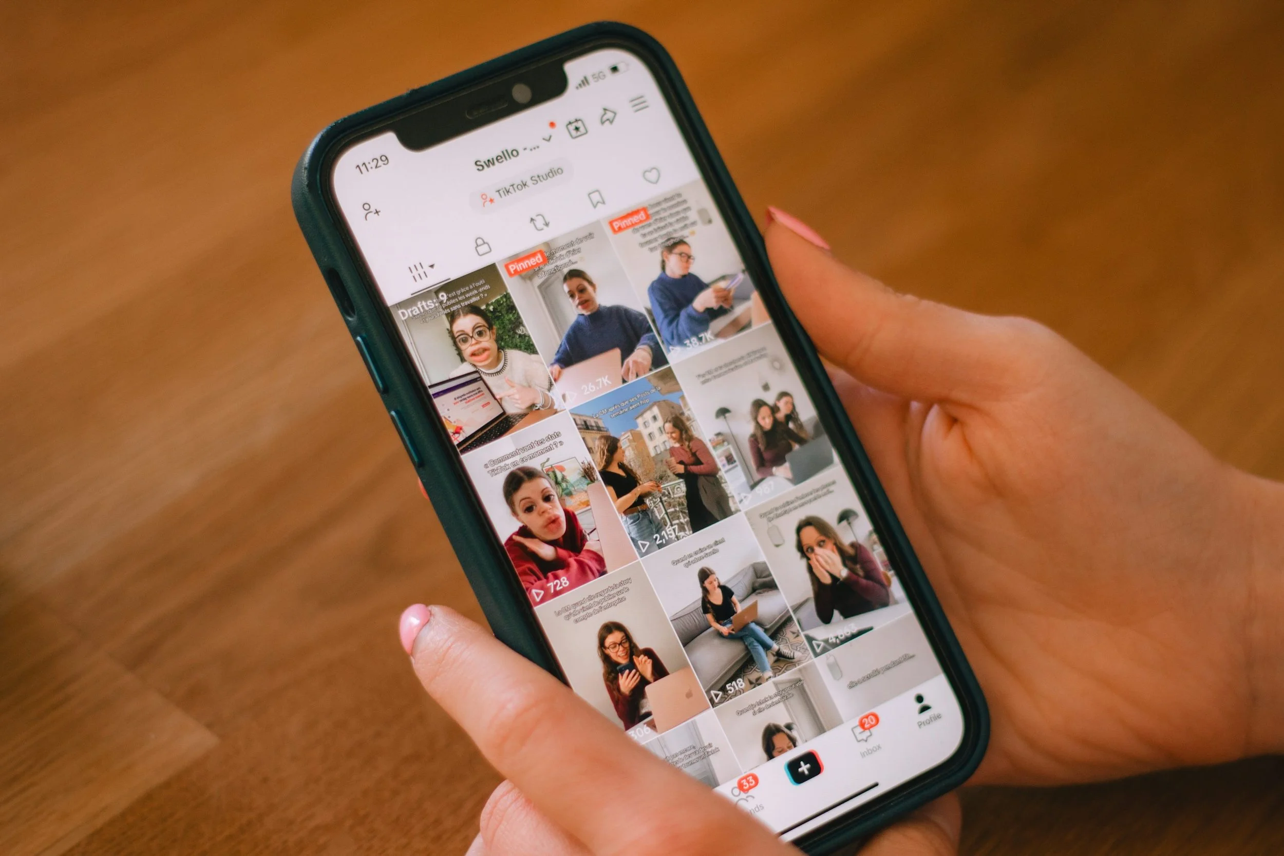 Hand holding a smartphone displaying a TikTok profile video grid on a wooden table
