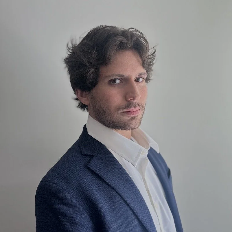 Portrait of a bearded man with wavy dark hair wearing a navy blazer and white shirt