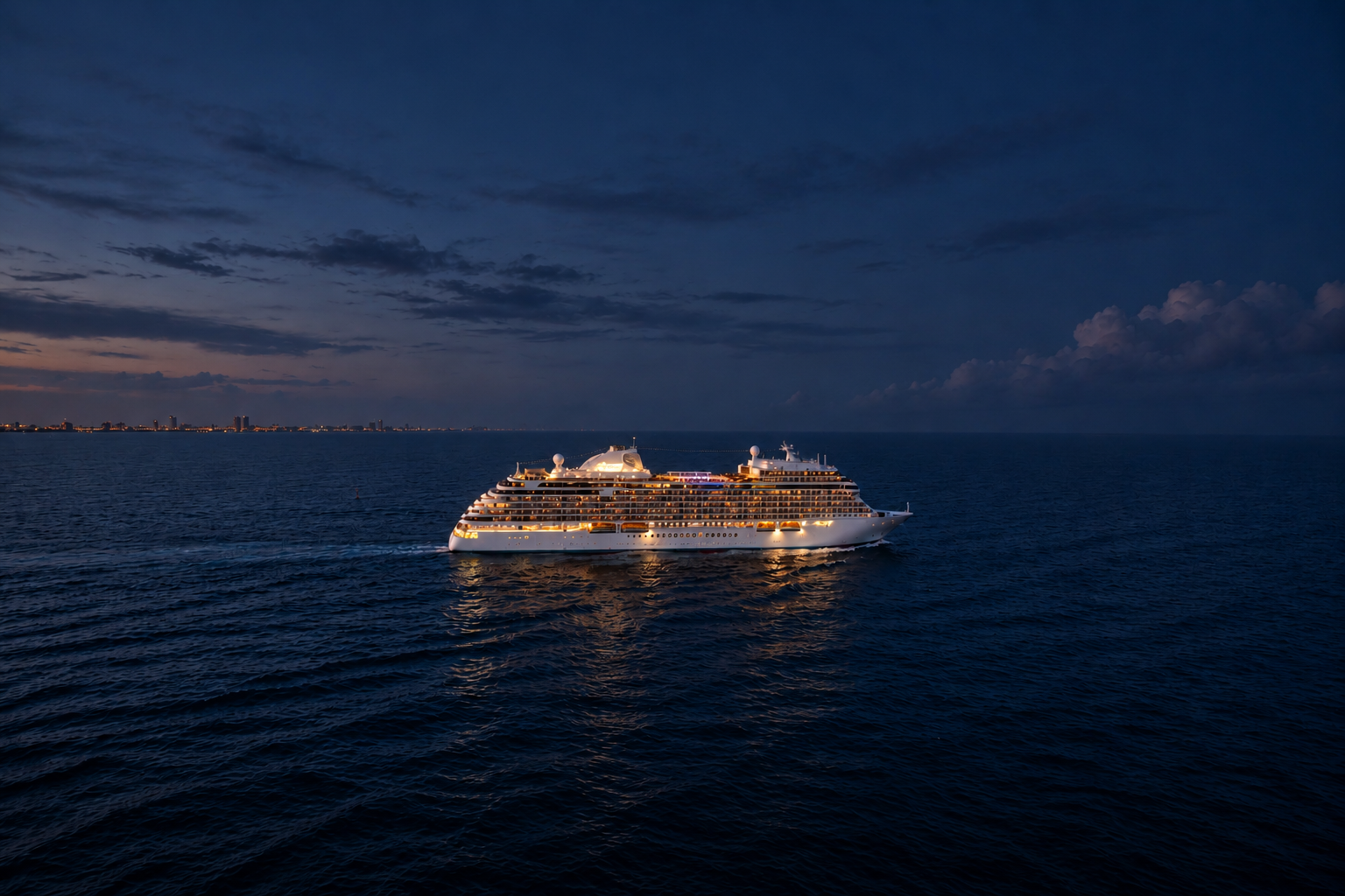 Regent Explorer cruise ship illuminated at night sailing on calm ocean waters.
