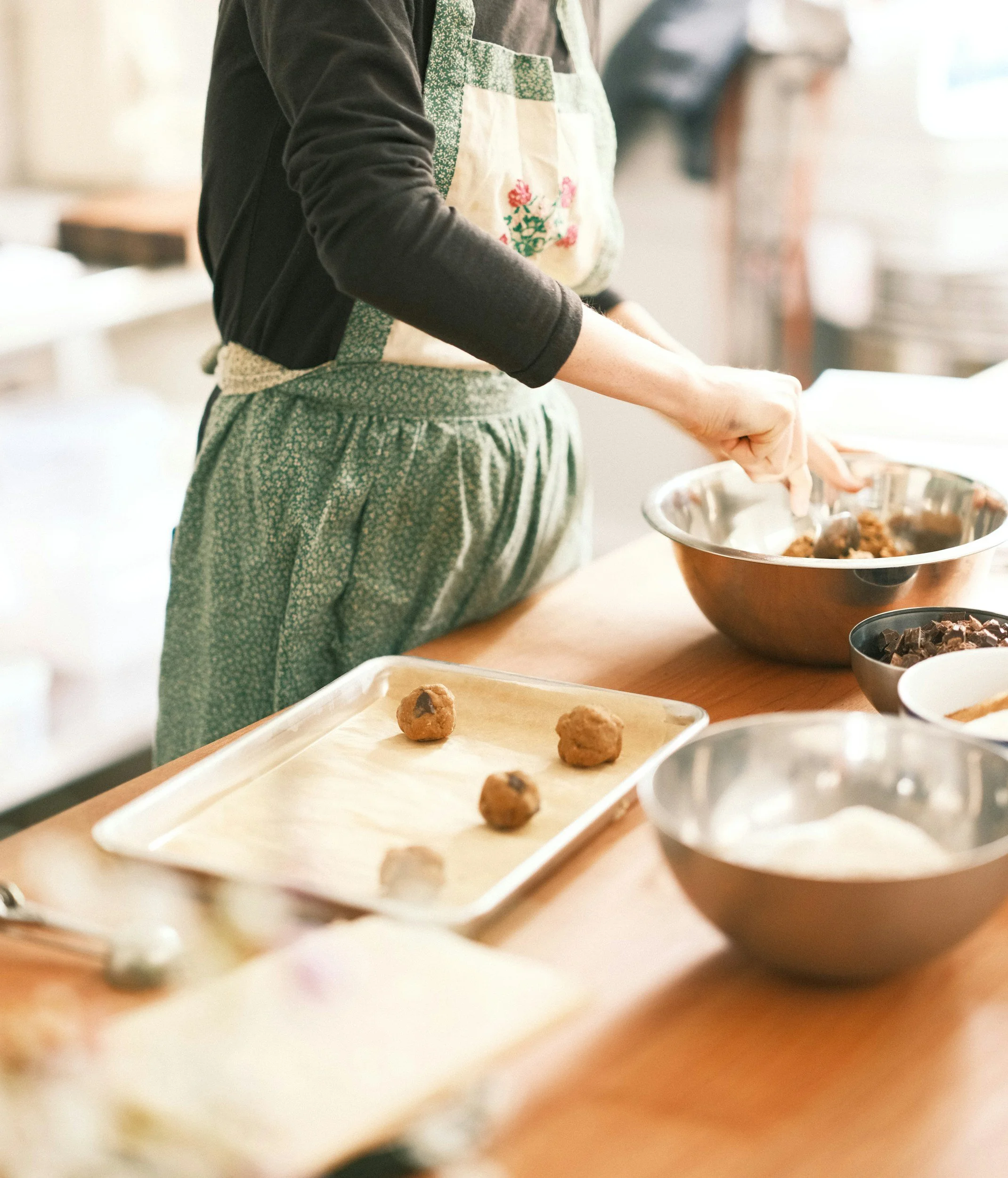 Person wearing patterned apron baking cookies on a tray in a kitchen.