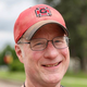 The author of a book about slavery, the Civil War, and American exceptionalism who is wearing a Grinnell College cap and smiling.