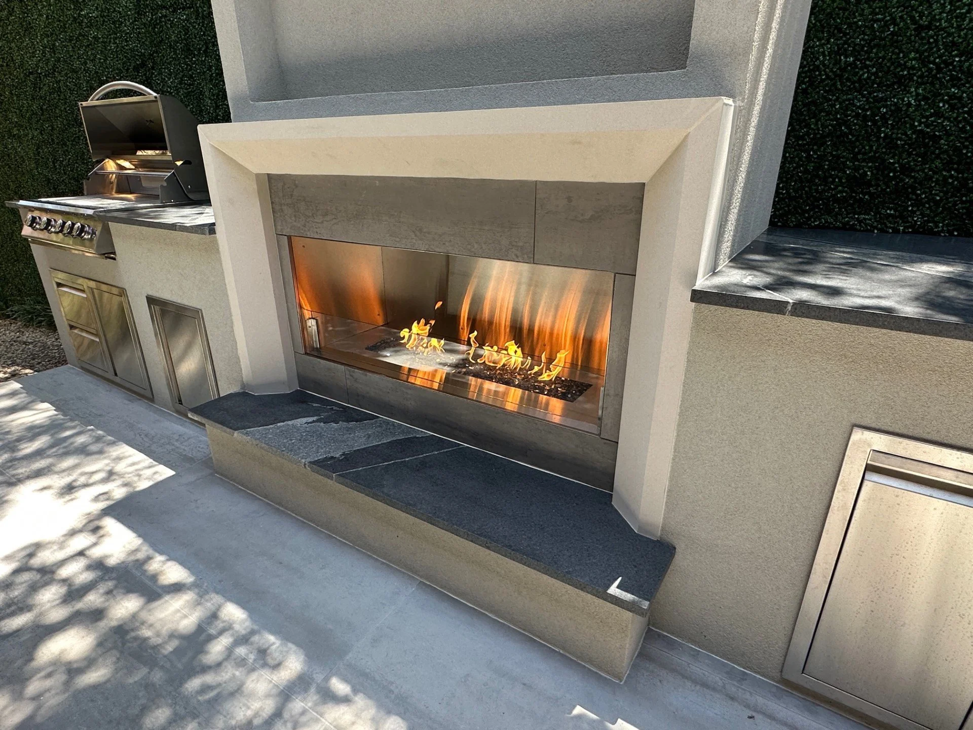 Modern linear gas fireplace with stone hearth bench and outdoor kitchen