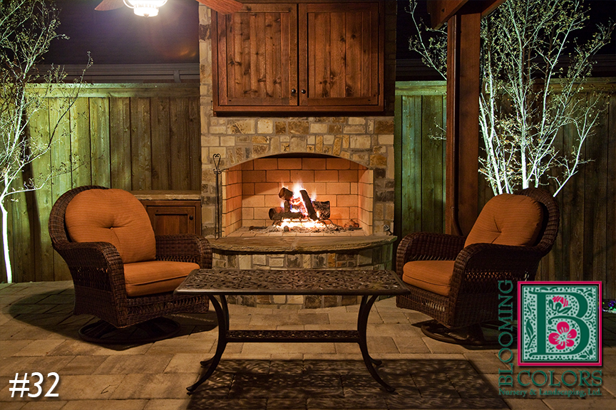 Outdoor stone fireplace with glowing fire and wicker chairs at night